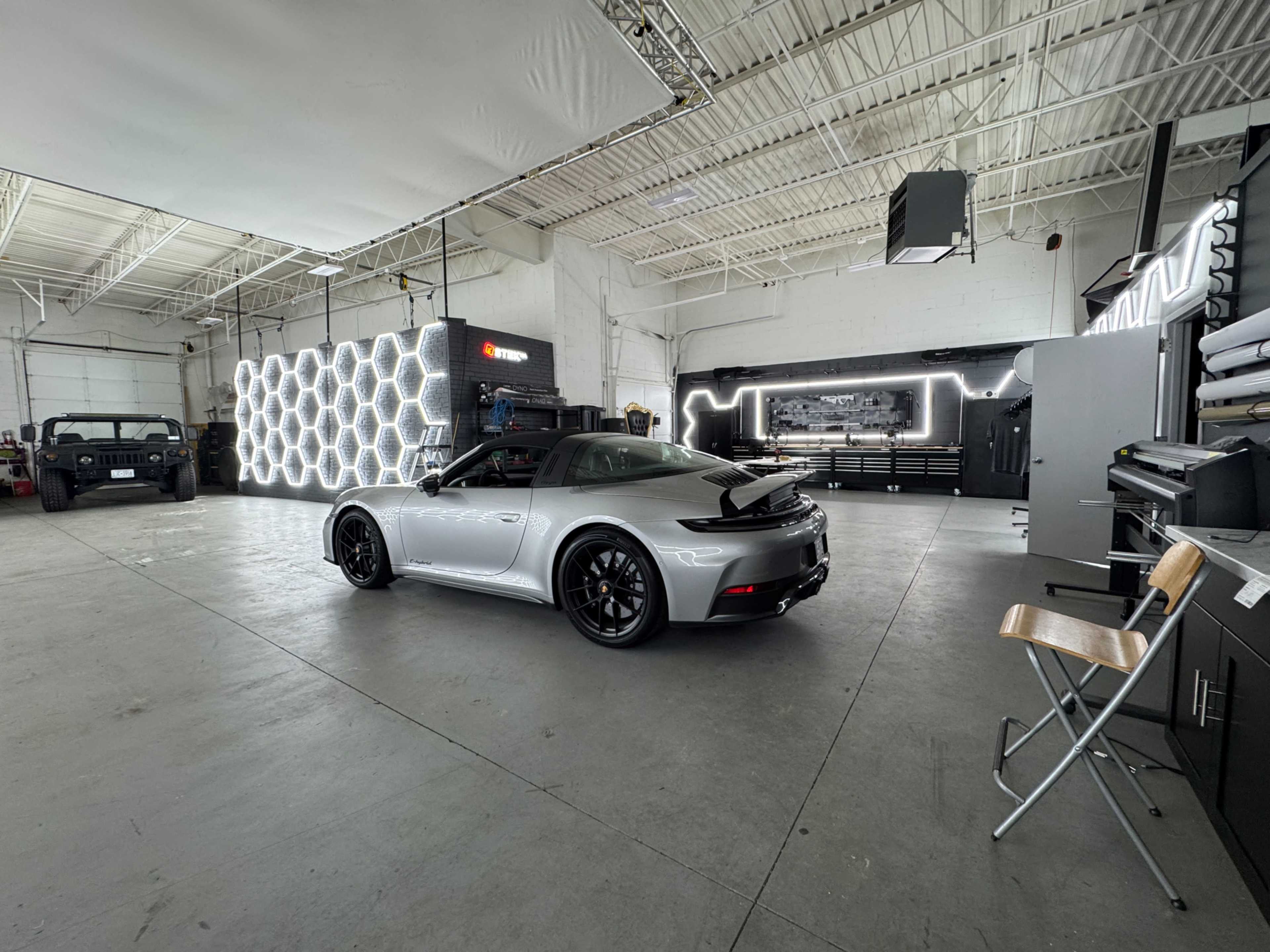 A sleek silver sports car is parked in a spacious modern garage that features a hexagonal light installation and various tools on display.