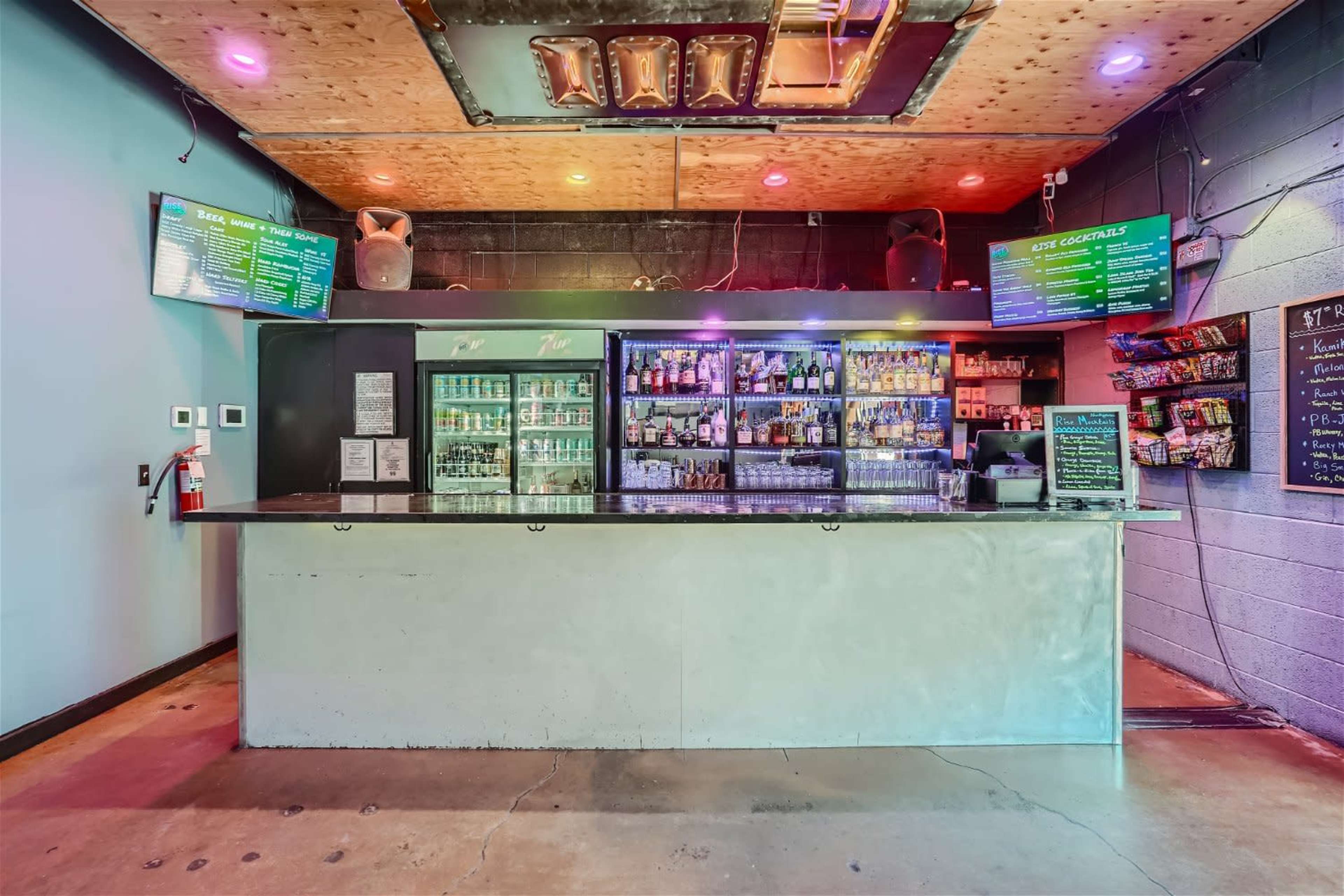 The image shows a bar area with a long counter, shelves stocked with various drinks, and a menu displayed above the bar.