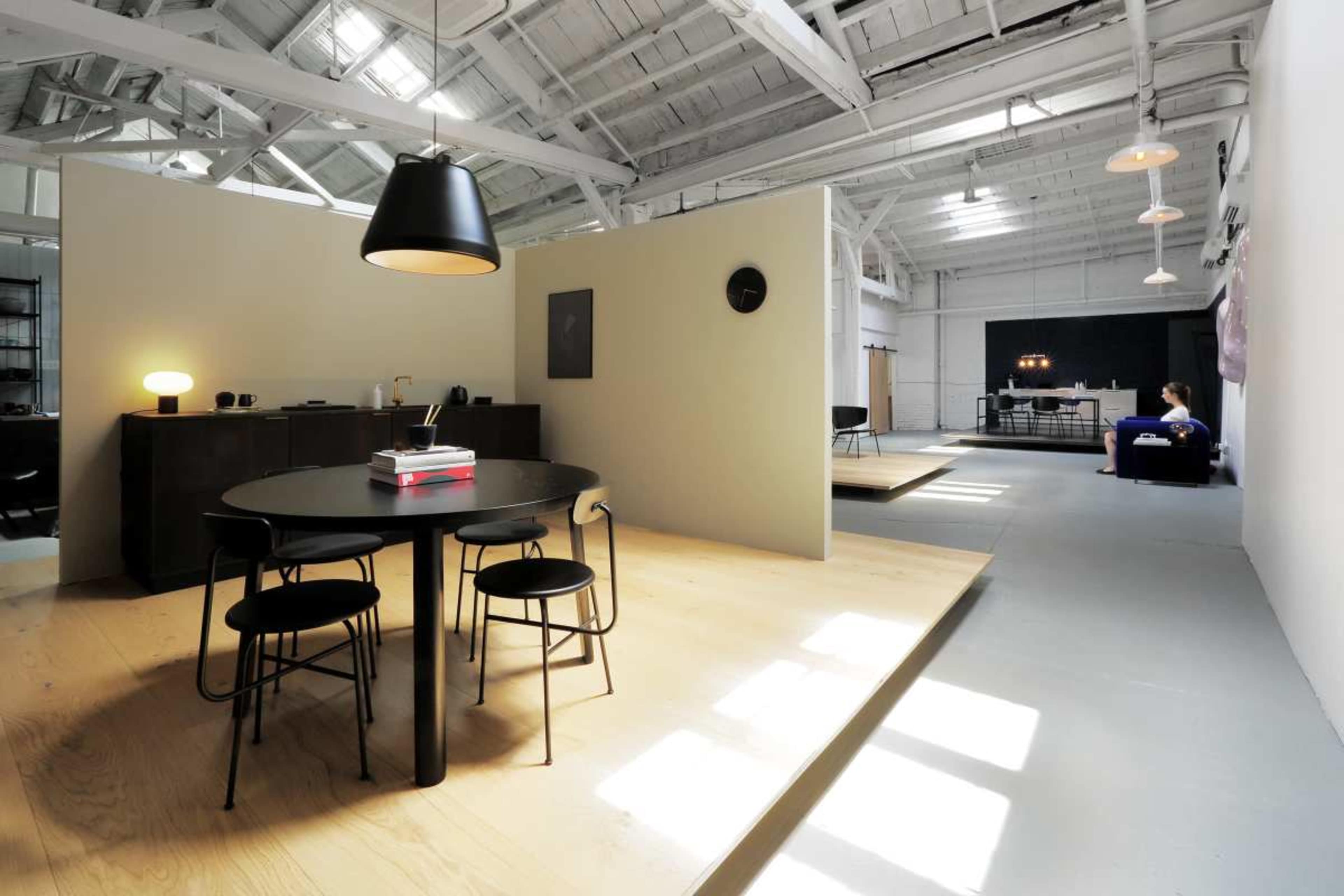 The image depicts a modern, open-concept living space featuring a dining area with a round table and four chairs, separated by a partition from a lounge area with a sofa.