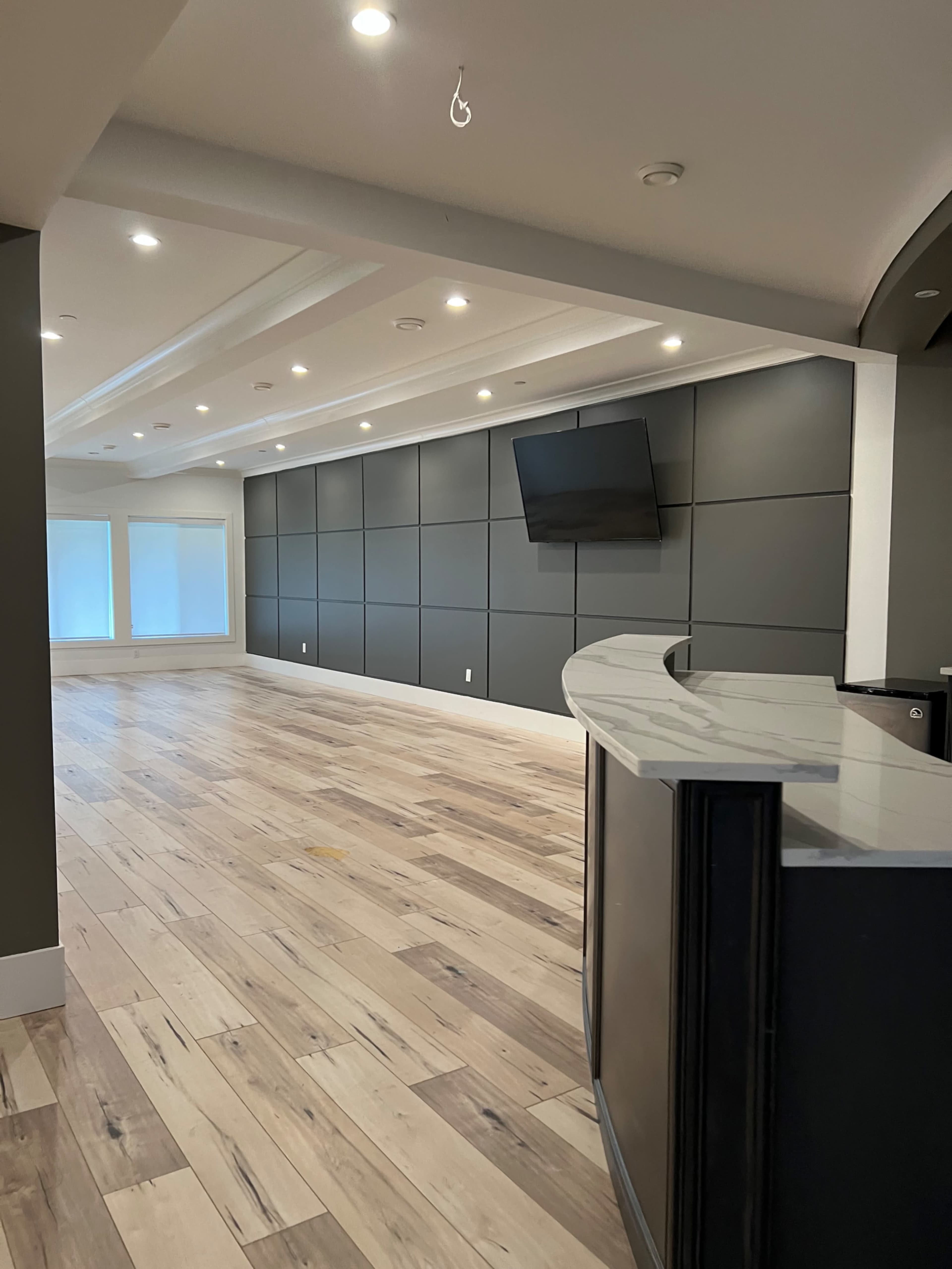 A spacious, modern interior with a curved reception desk, a flat-screen TV on the wall, and large windows letting in natural light.
