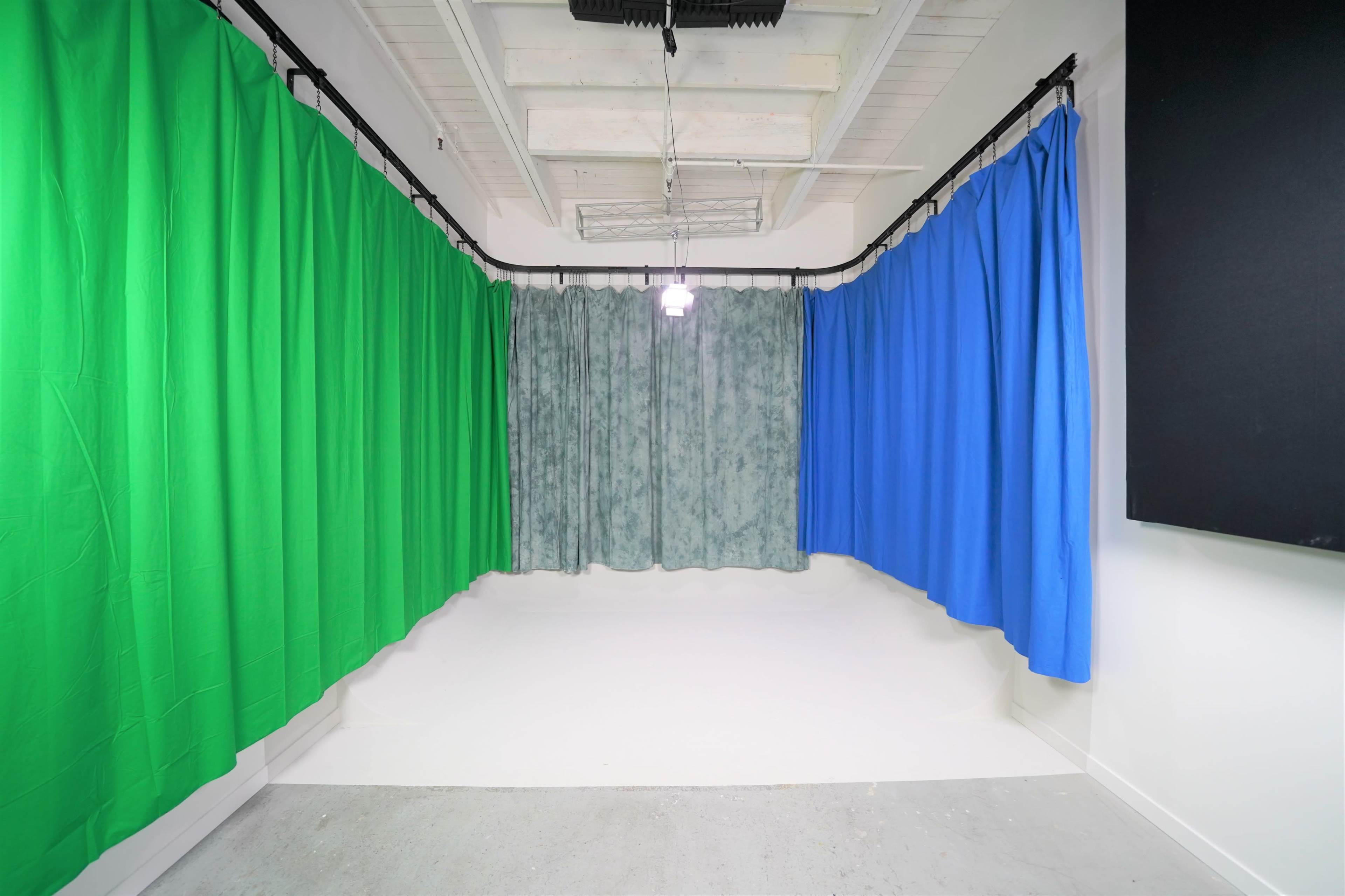 A room features multiple curtains in green, blue, and gray, surrounding a white floor and illuminated by overhead lighting.