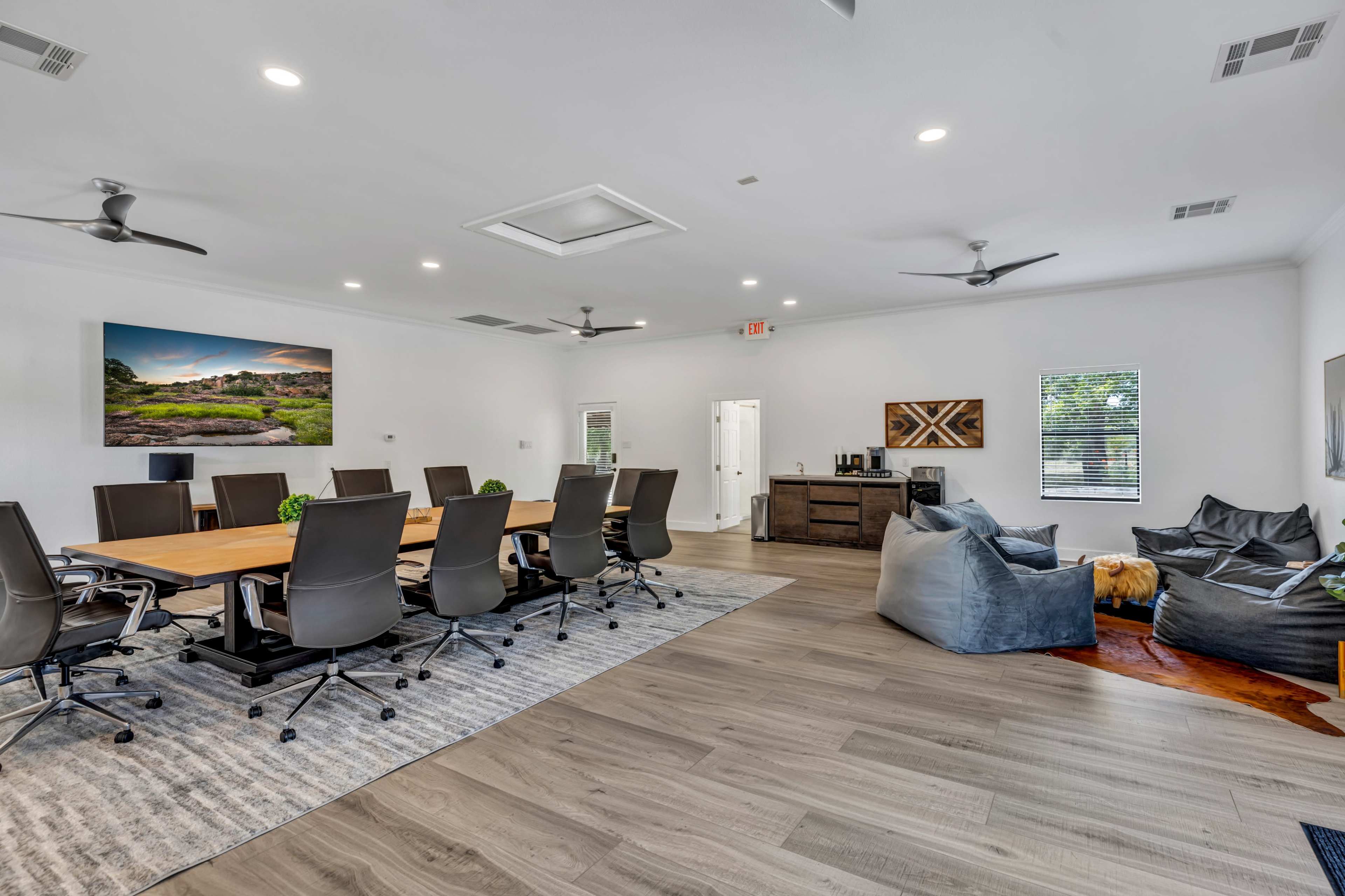 A modern conference room features a large table surrounded by ergonomic chairs, with a kitchenette area and a cozy seating space.