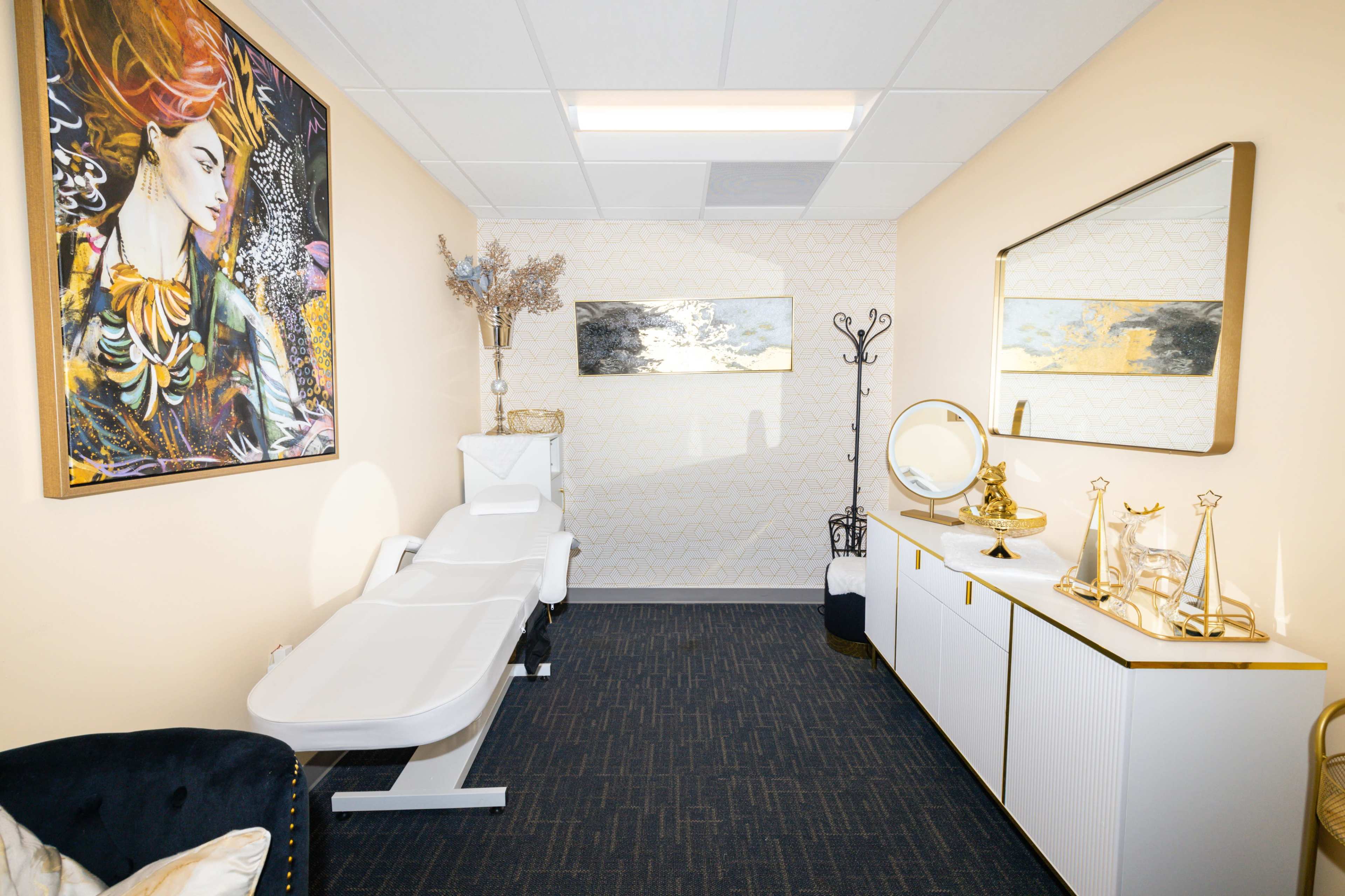 The image shows a serene treatment room featuring a massage table, a decorative mirror, and modern artwork on the walls.