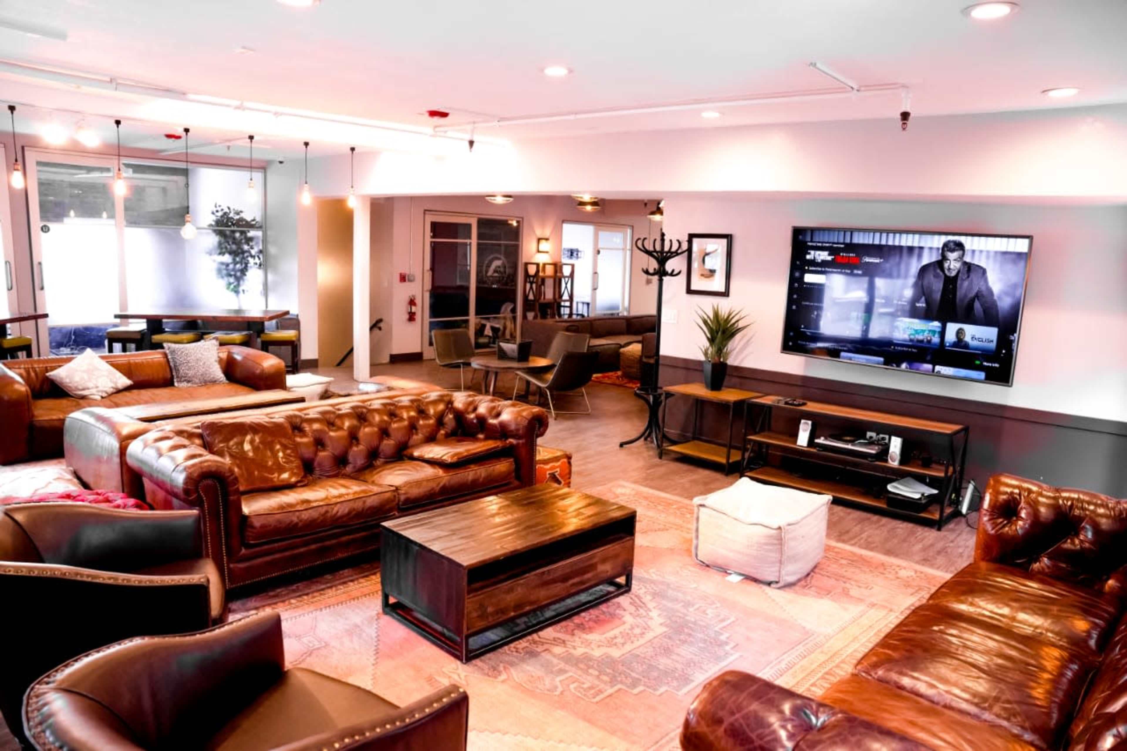 A modern lounge area featuring leather sofas, a coffee table, and a large TV mounted on the wall.