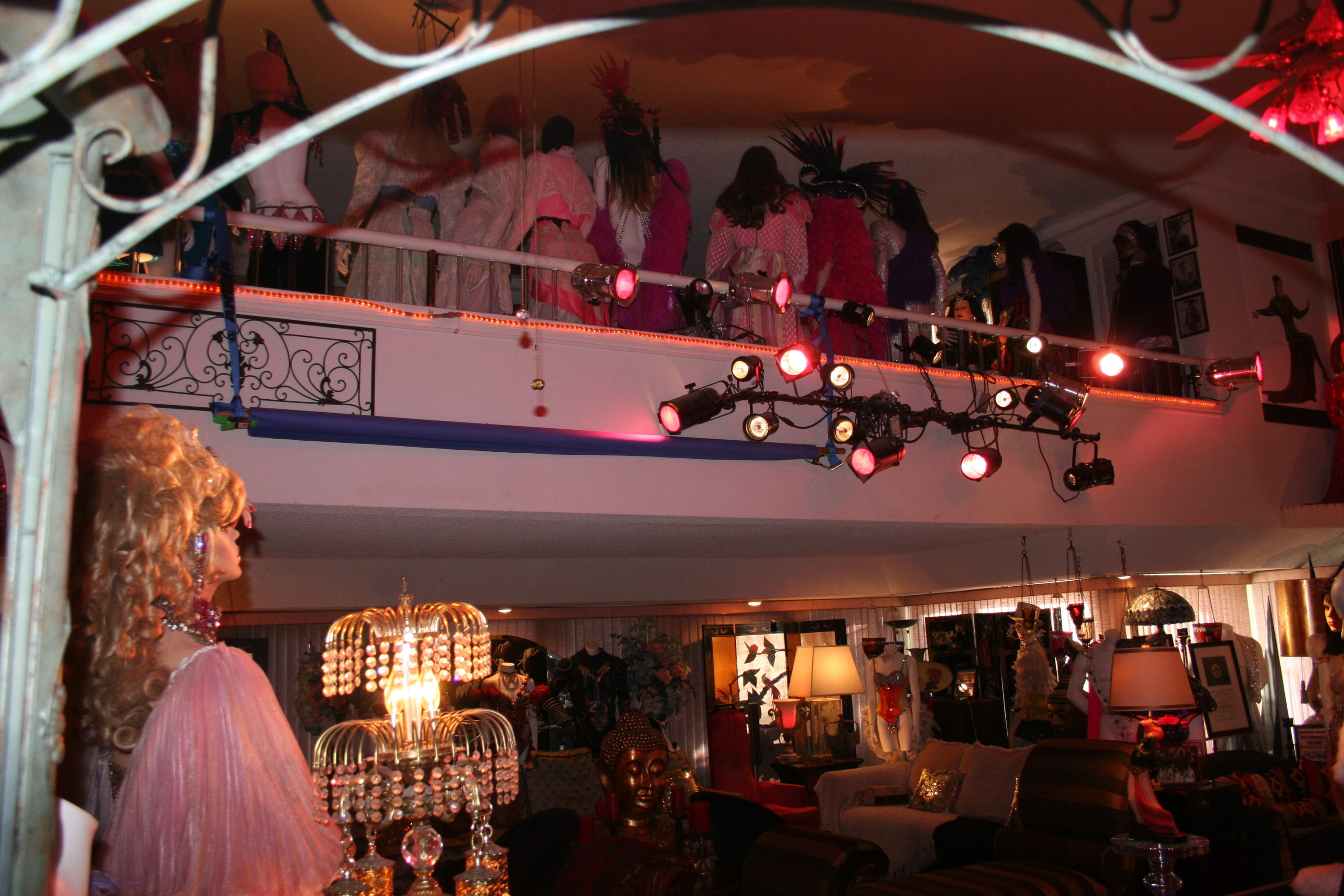 The image shows an eclectic interior with mannequins on a balcony and various decorative items throughout the room.