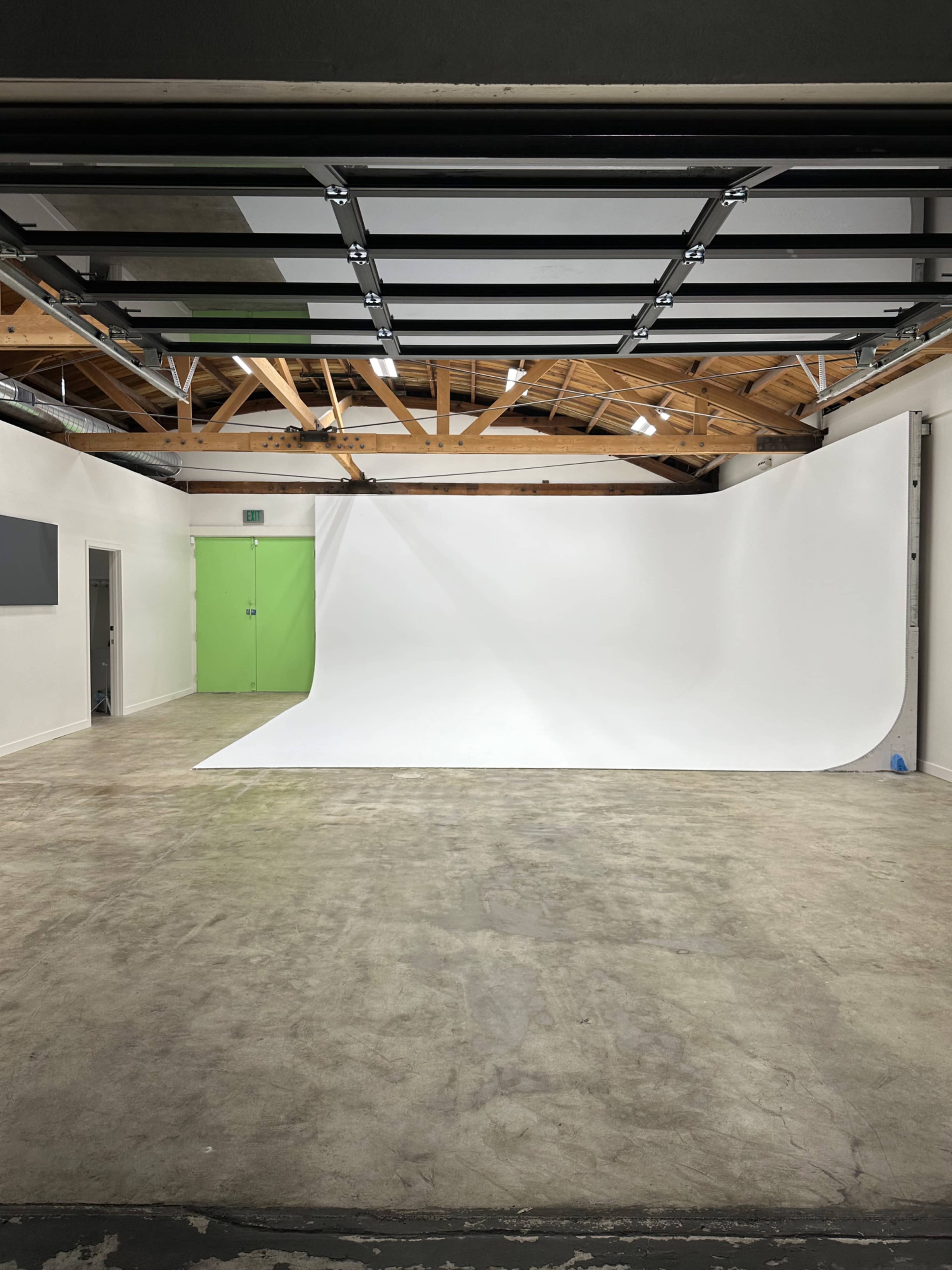 A spacious photography studio with a seamless white backdrop, a concrete floor, and a green door.