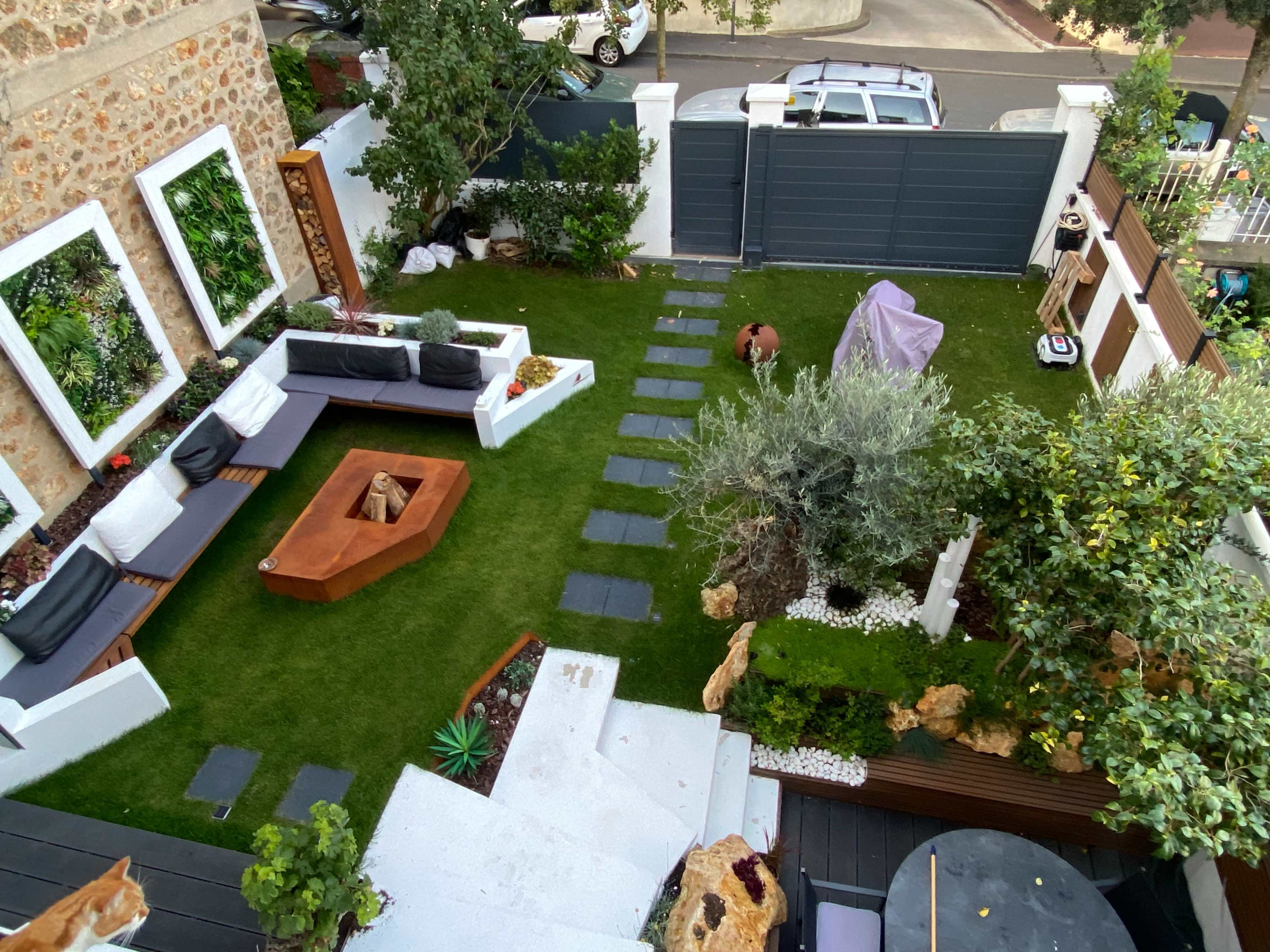 An outdoor garden space featuring a well-maintained lawn, a fire pit, a seating area with modern furniture, and various plants and trees.