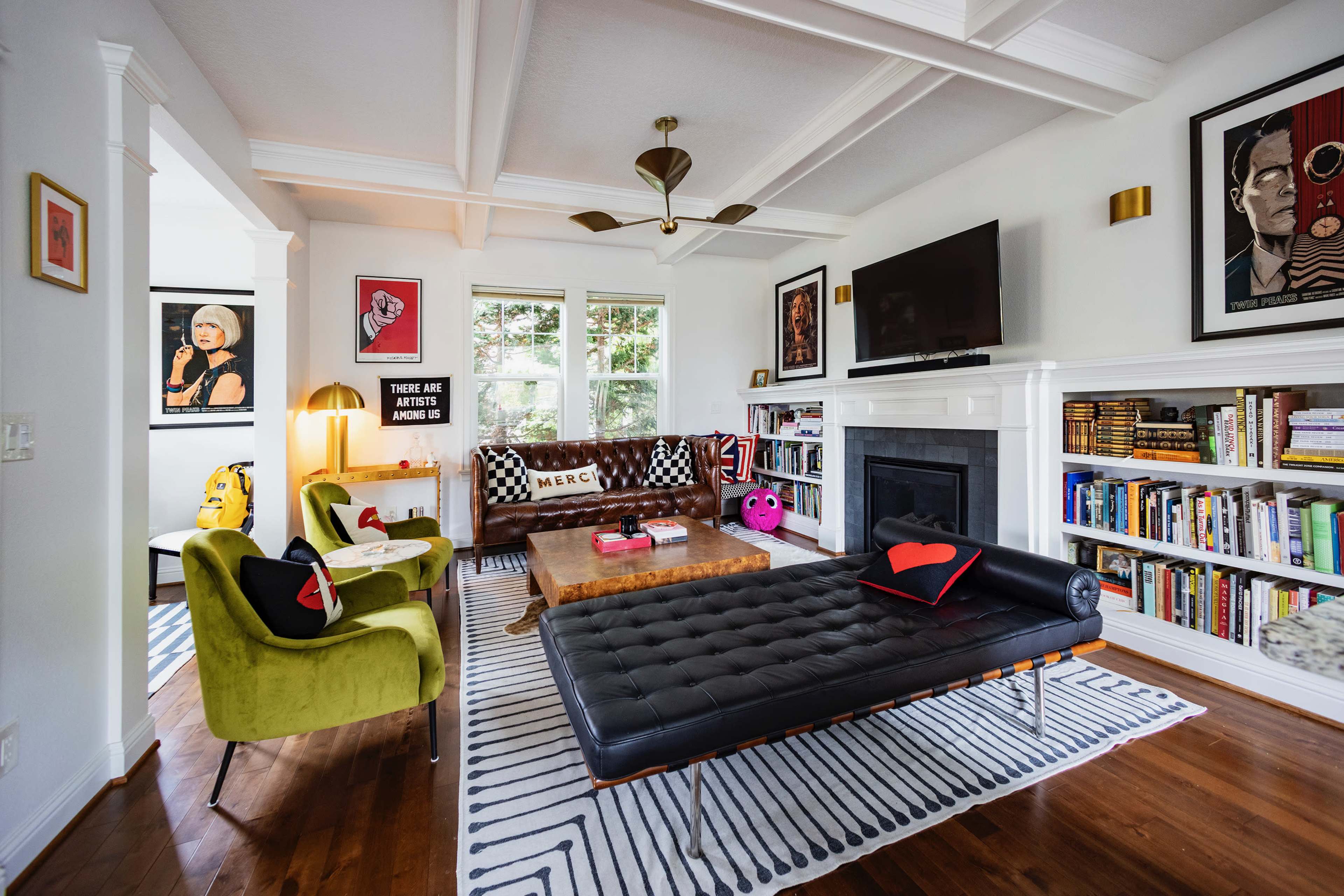 The living room features a black leather sofa, a wooden coffee table, and a bookshelf, along with various wall art and a large television.