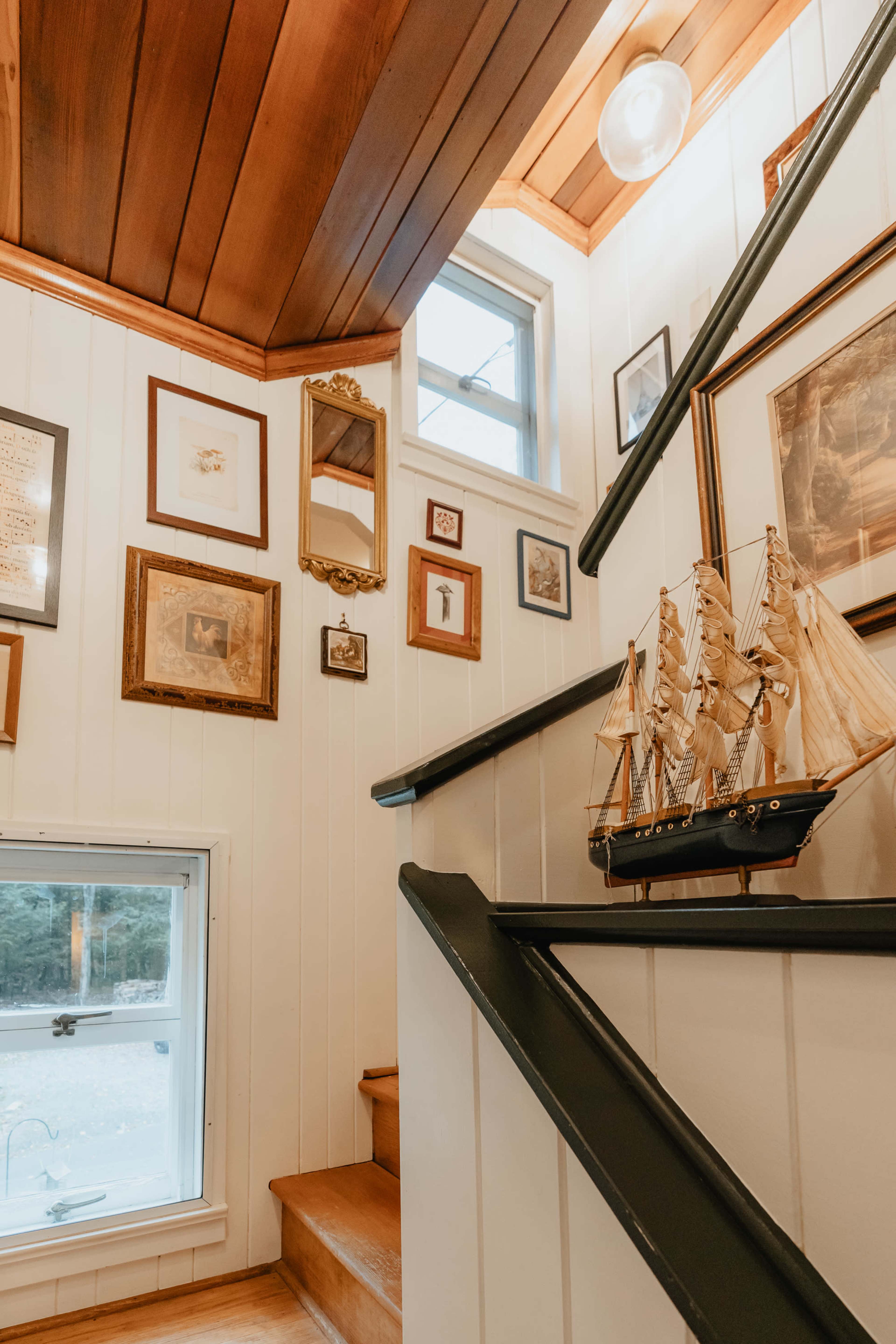 A wooden staircase leads up to a landing adorned with framed artwork and a decorative ship model on the wall.