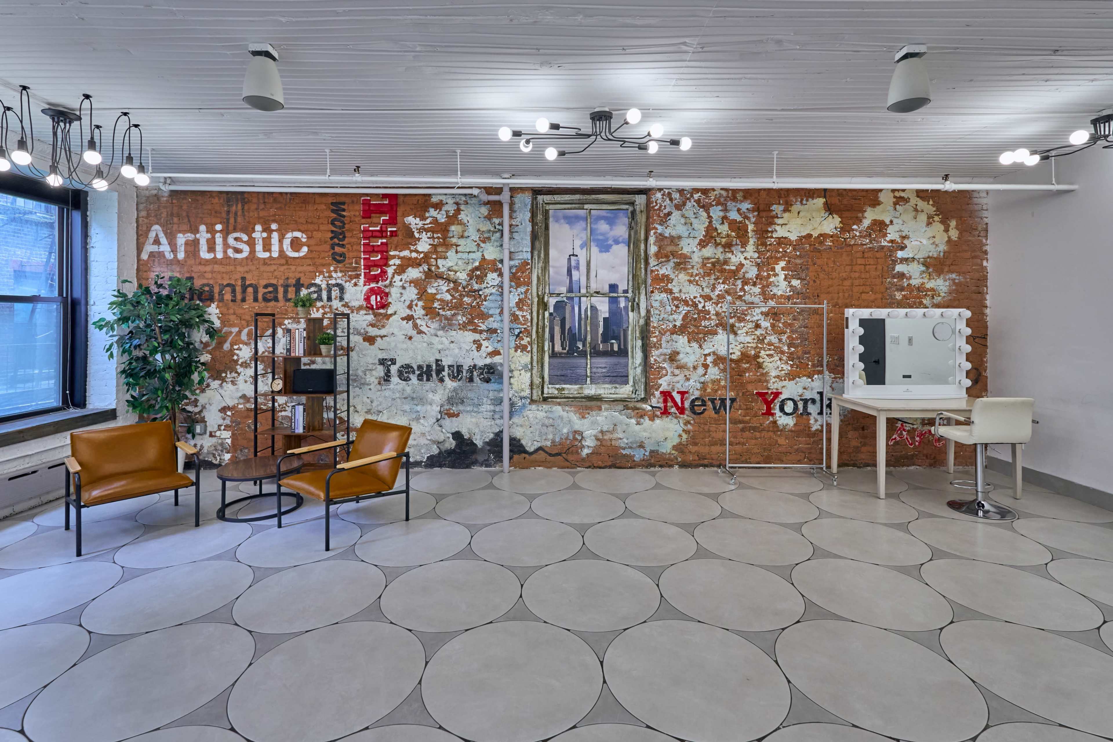 A spacious room with a rustic brick wall featuring the words "Artistic" and "New York," complemented by modern furniture and circular floor tiles.
