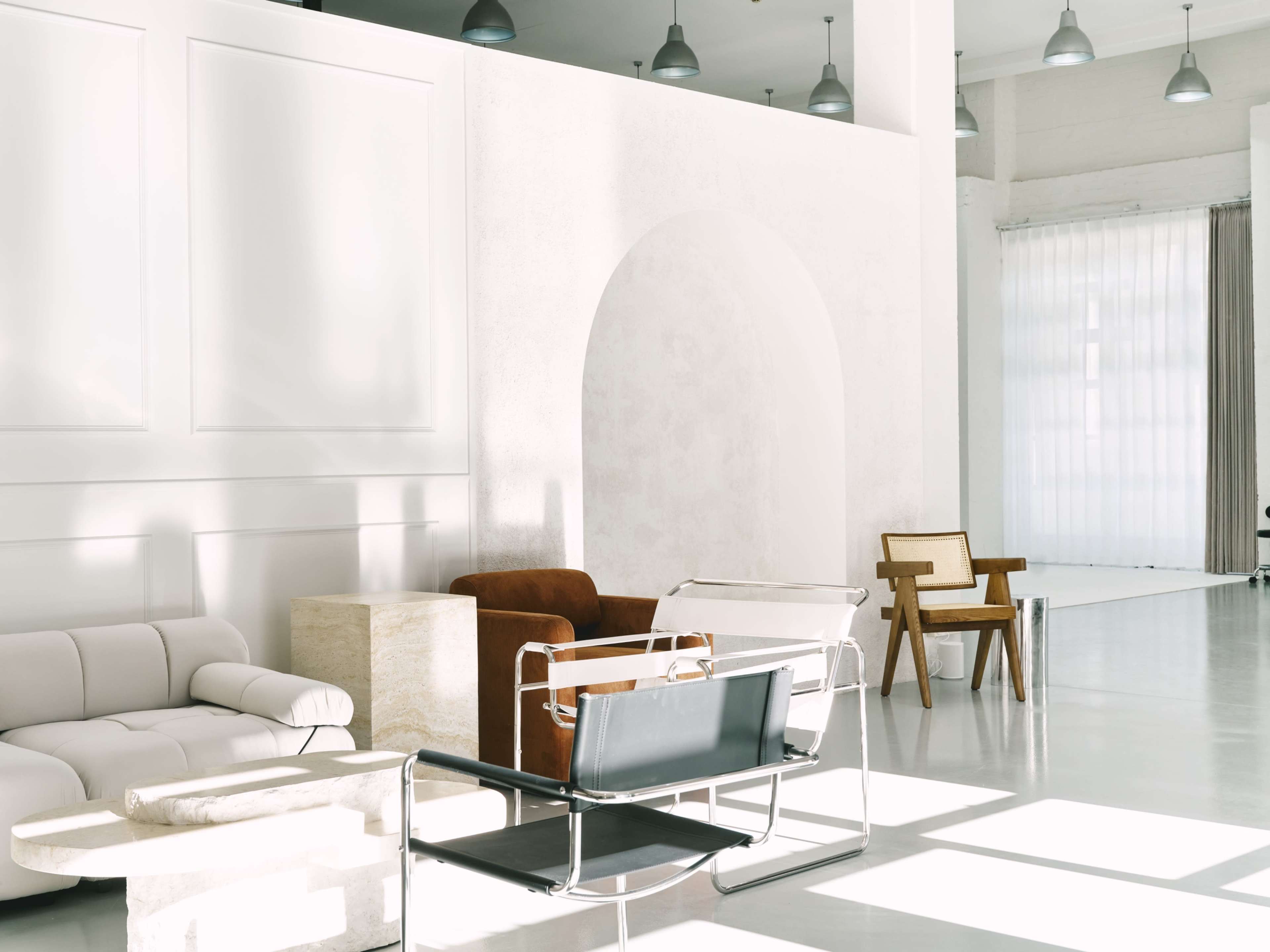 The image features a minimalist interior with various modern seating options arranged in a bright, spacious room.