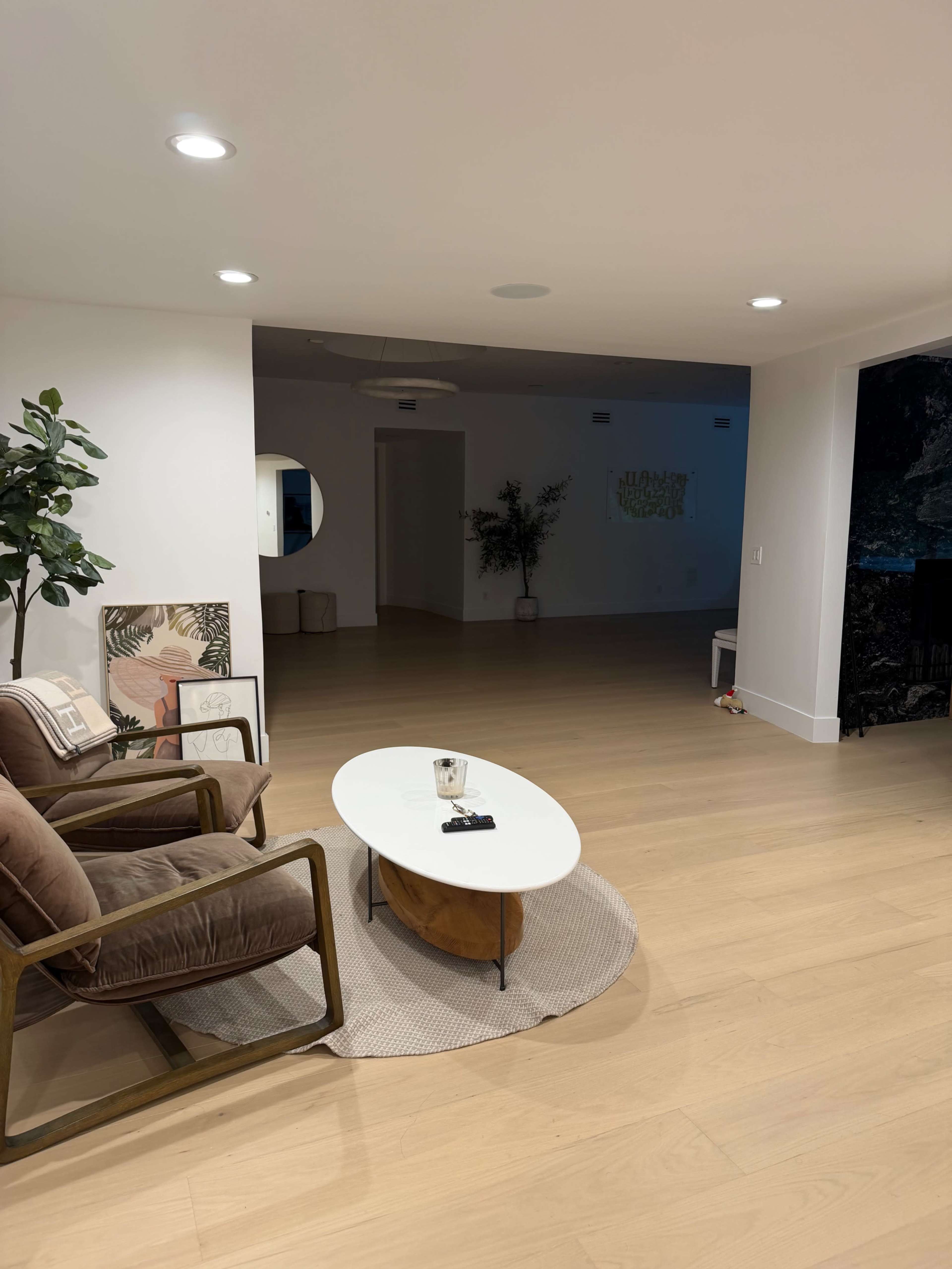 The image shows a spacious living room with a coffee table in the center, two armchairs, and a decorative plant in one corner.