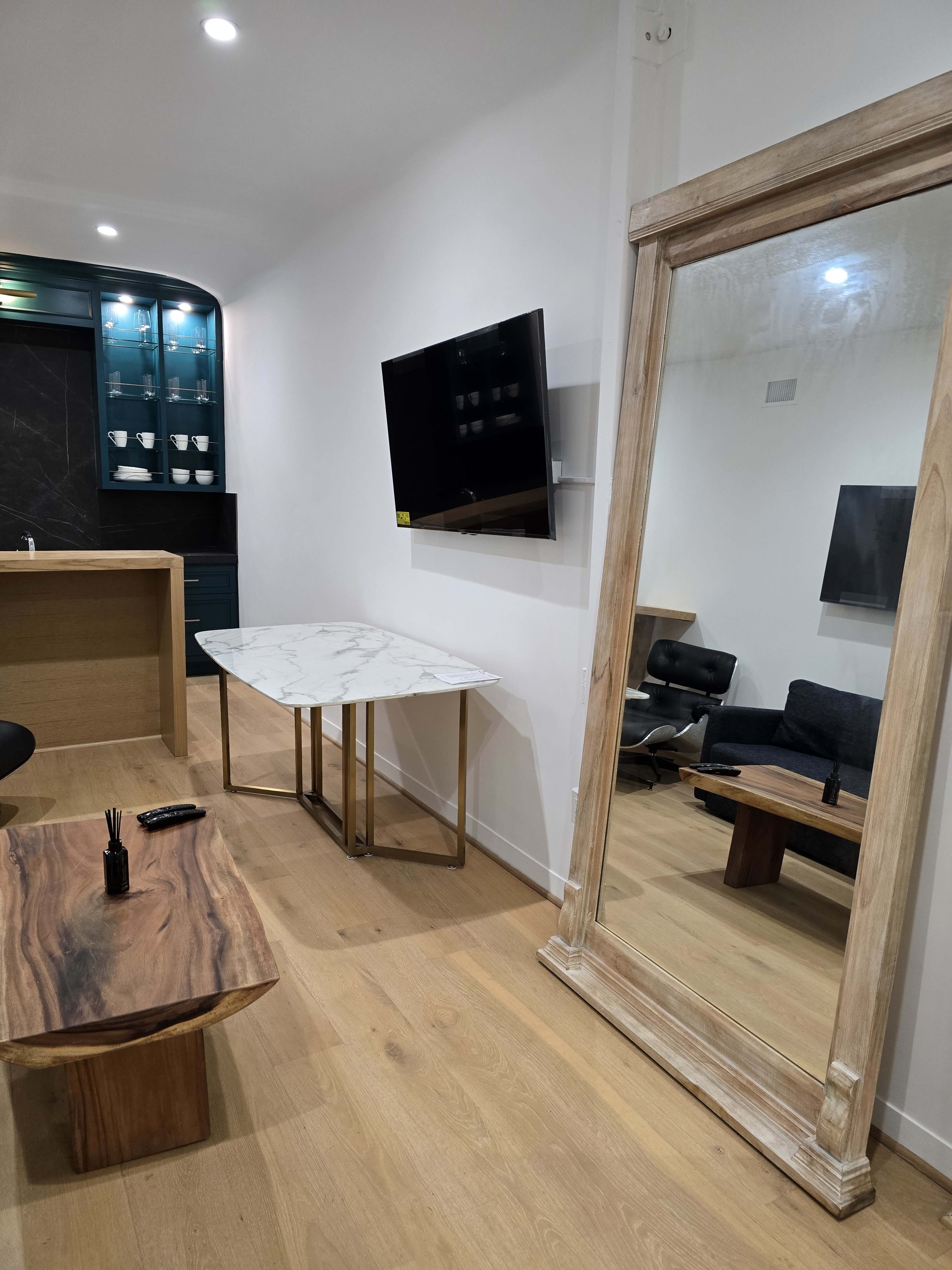 The room features a marble-top dining table, a large mirror, a wall-mounted television, and modern furniture, with light wood flooring and neutral-colored walls.