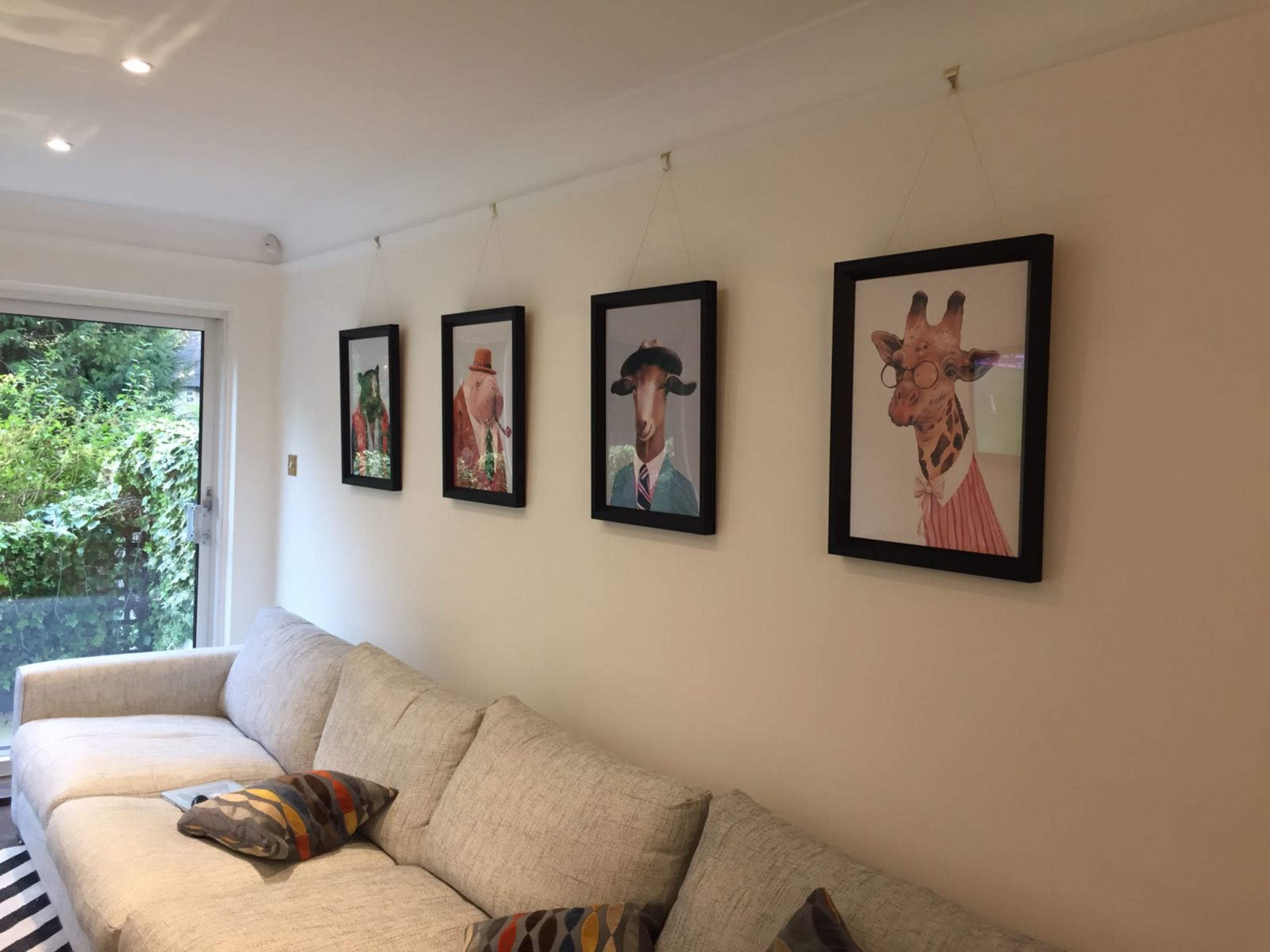 A living room with a light-colored sofa and five framed animal portraits hanging on a white wall, depicting animals dressed in human clothing.