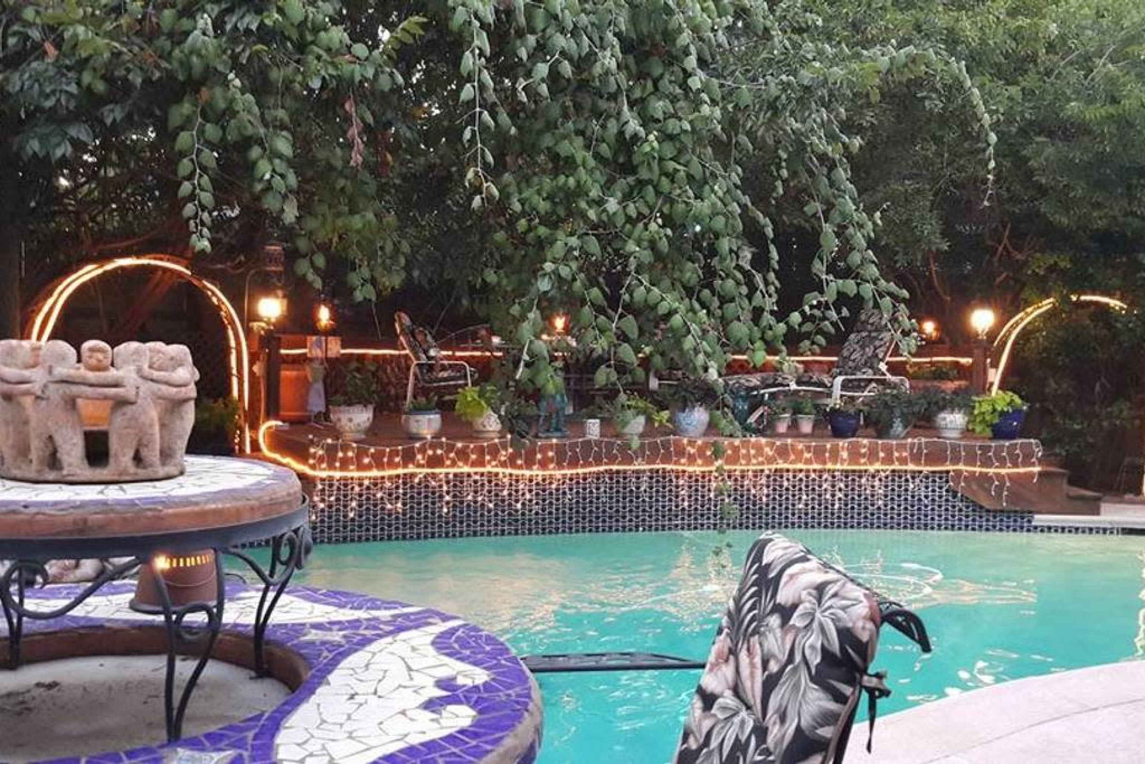 A pool area surrounded by greenery, with decorative lighting, a stone sculpture, and lounge chairs.