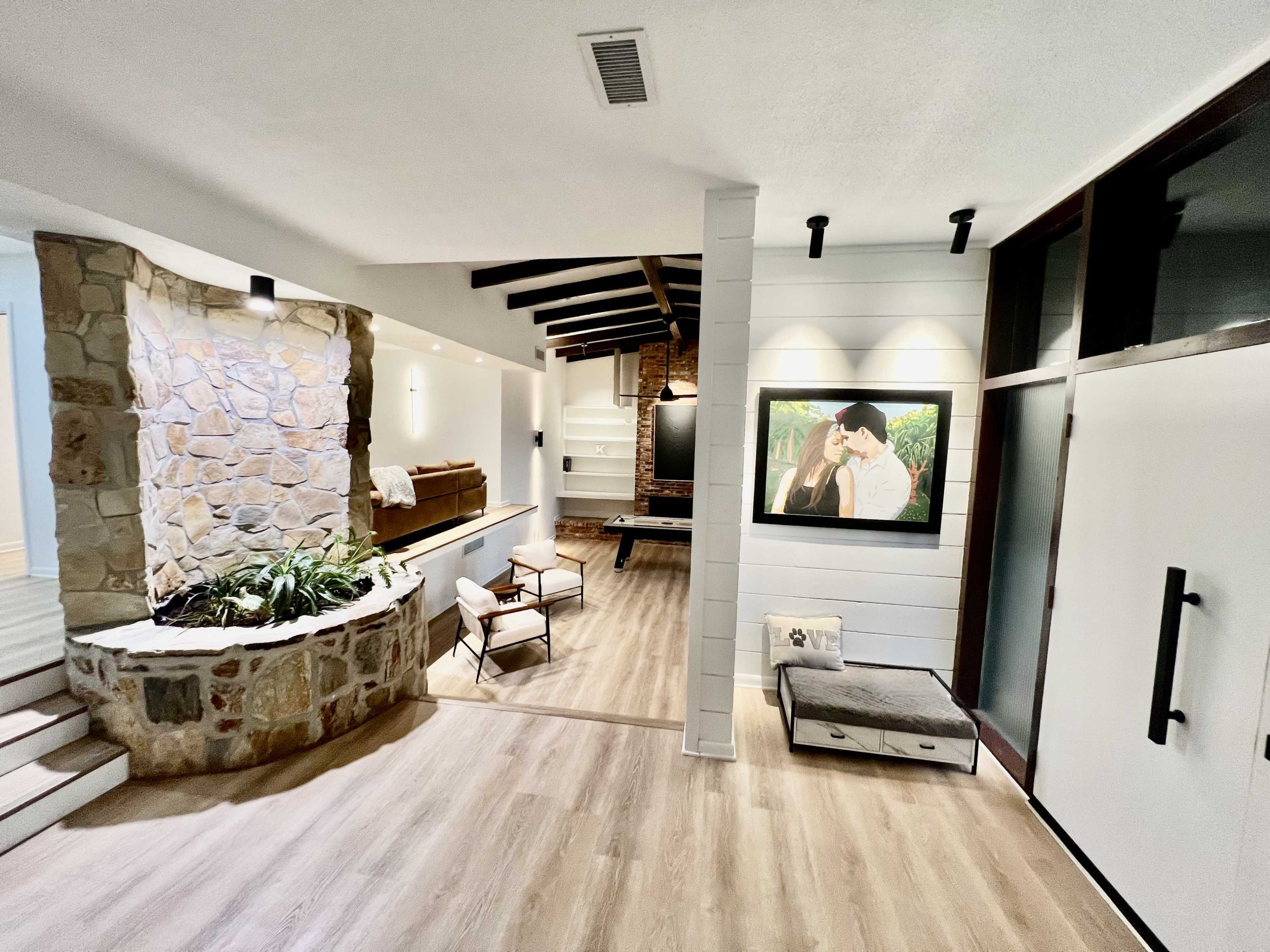 A modern interior space featuring a stone accent wall, wooden beams, and a large framed picture of a couple on one wall.