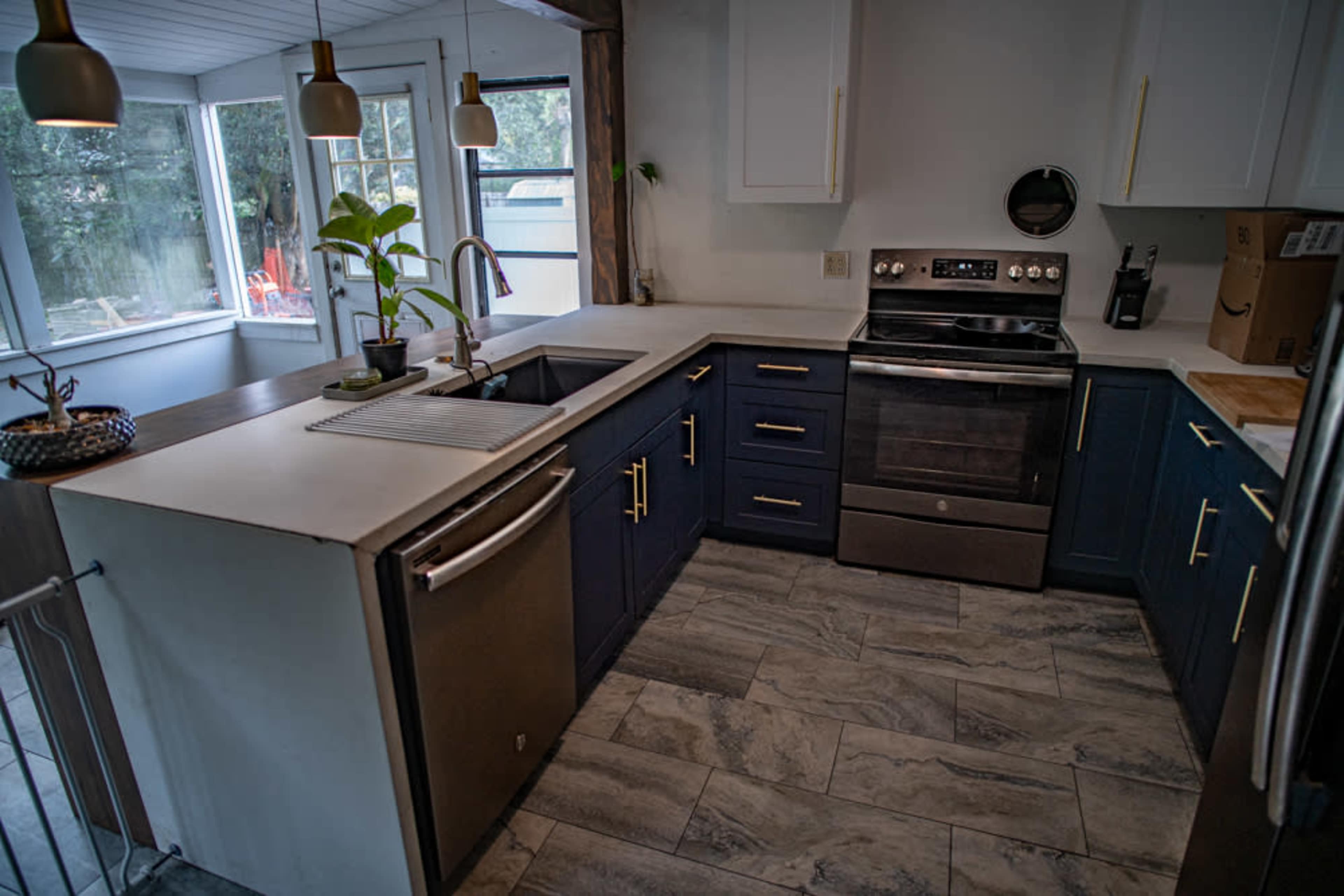 A kitchen features navy blue cabinets, a stainless steel oven, and a sink with a modern faucet, illuminated by pendant lights.