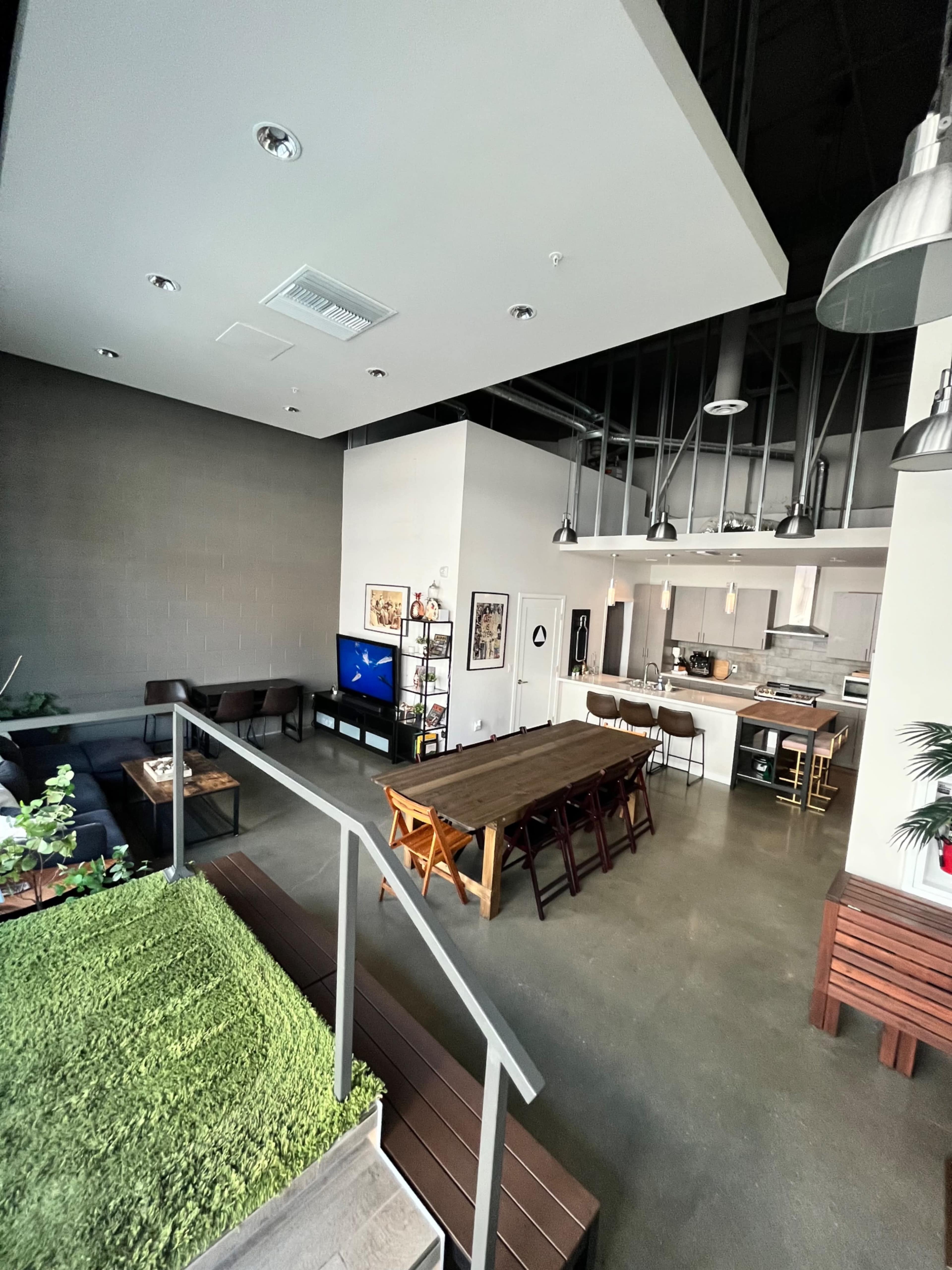 A spacious, modern open-concept living area with a dining table, kitchen, and lounge area featuring a television and indoor greenery.