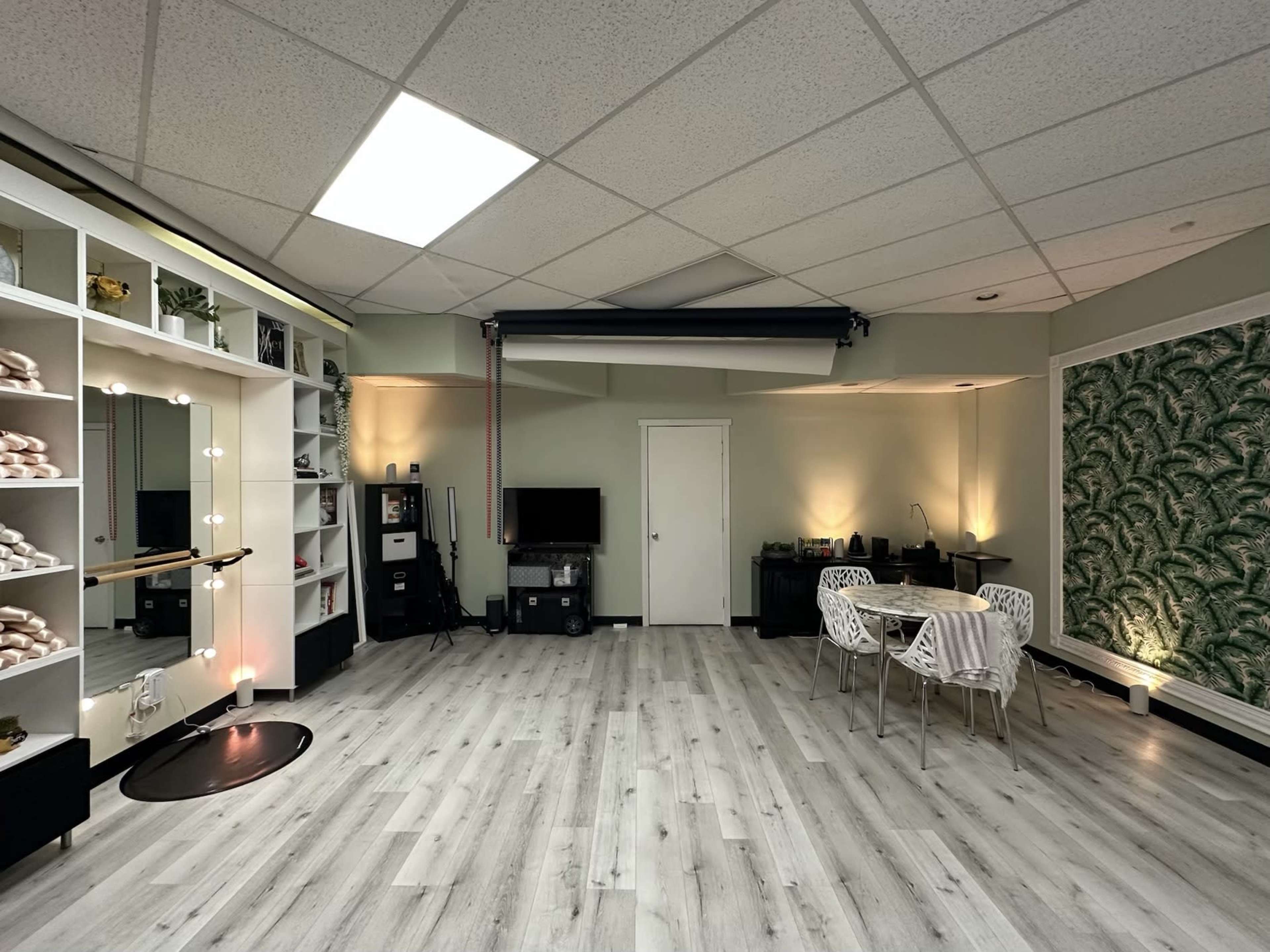 The image shows a well-lit studio space featuring a mirrored wall, a television, and a round table with four chairs surrounded by decorative accents.