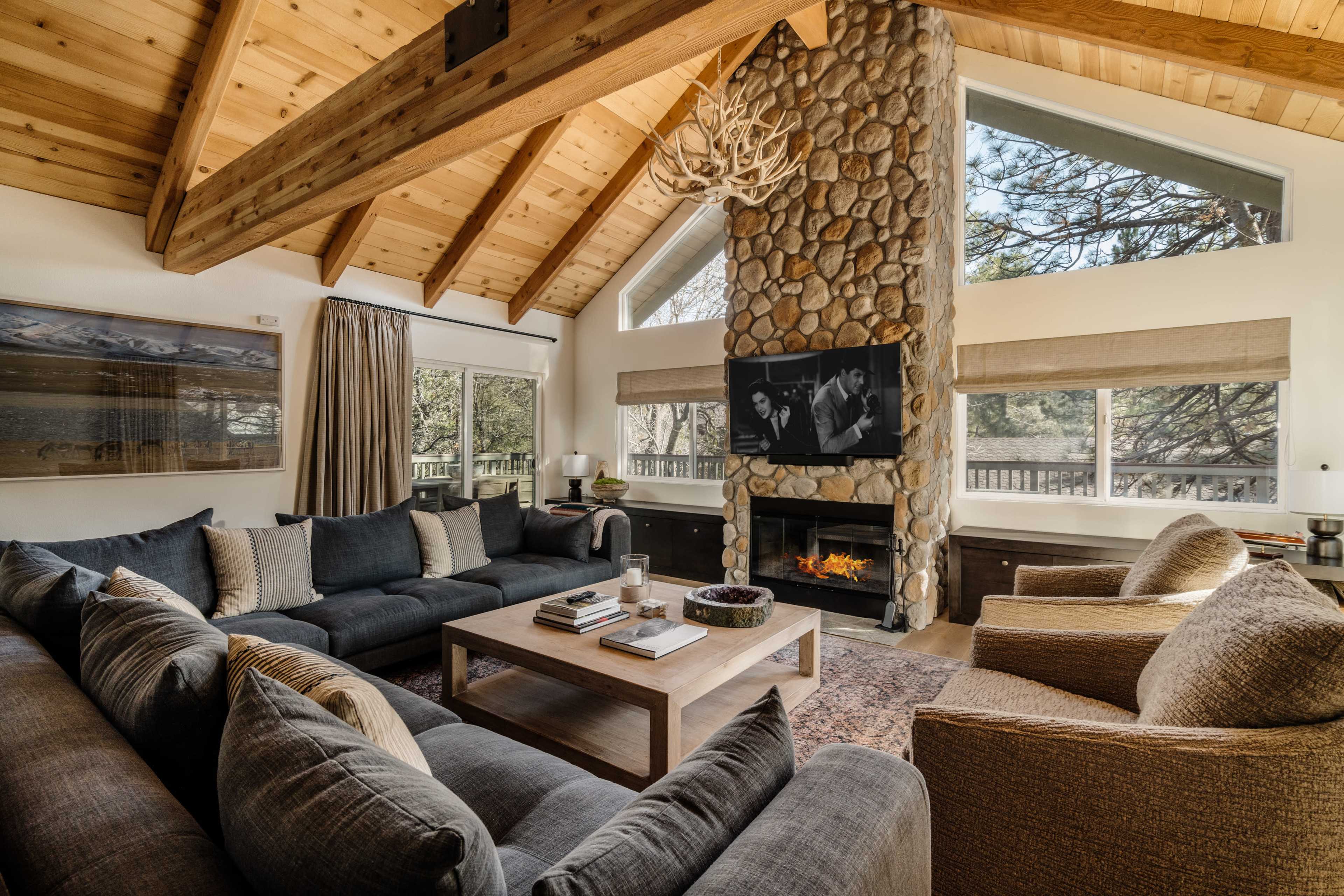 The living room features a large stone fireplace, vaulted wooden ceilings, and a sectional sofa arranged around a coffee table.