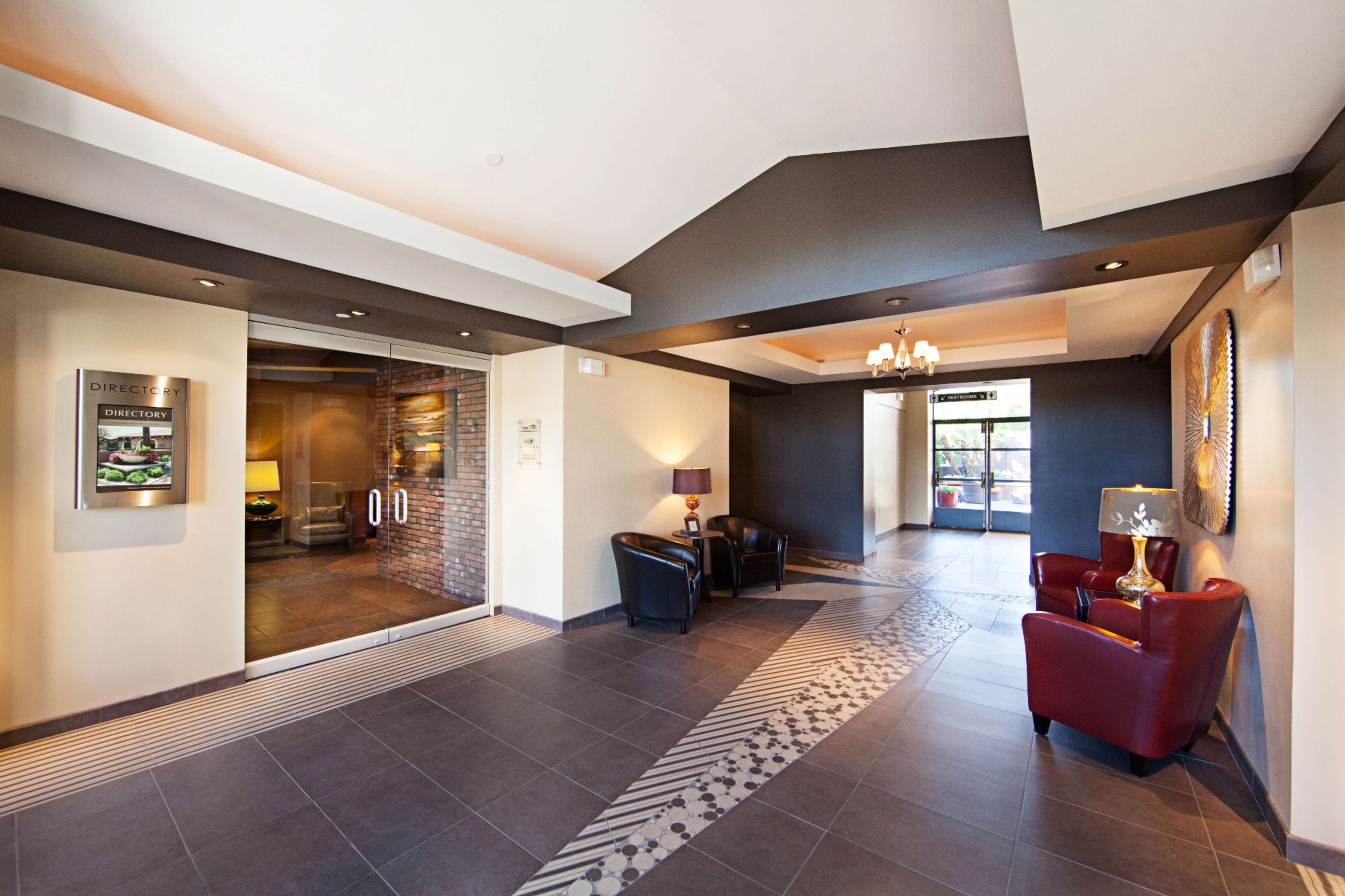 A modern lobby area featuring two leather chairs, a small table, and a reception area with glass doors leading outside.