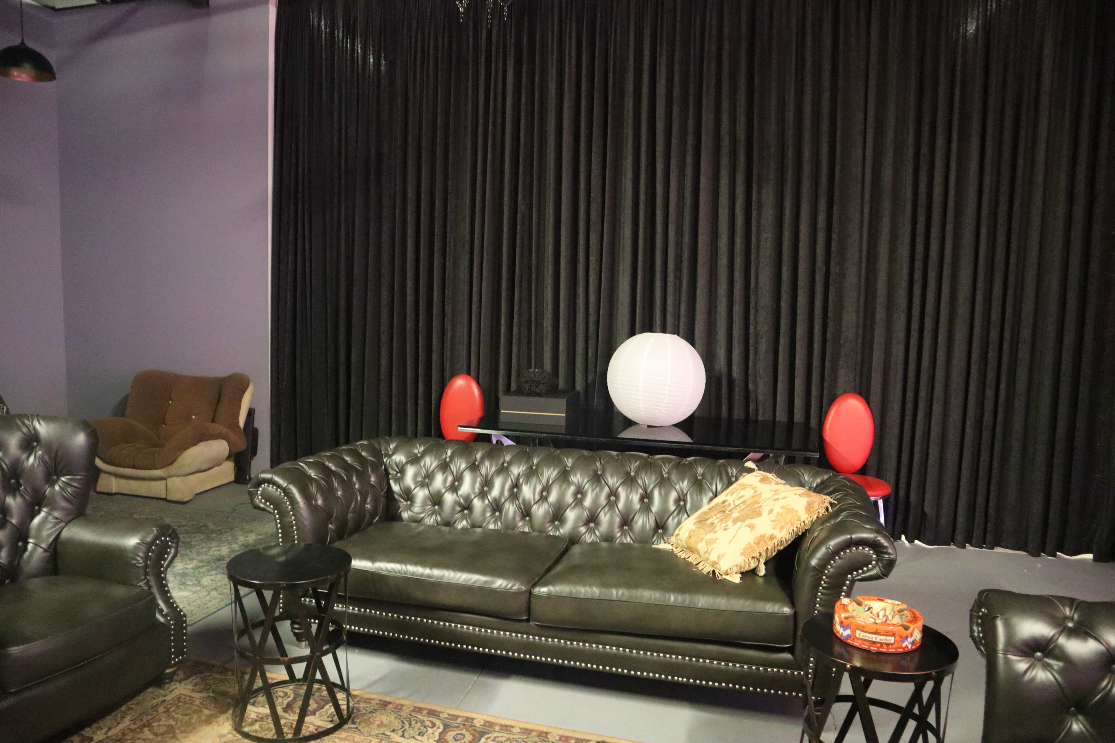 A living space with a dark curtain background, a black leather sofa, a small table, and a modern white lamp.