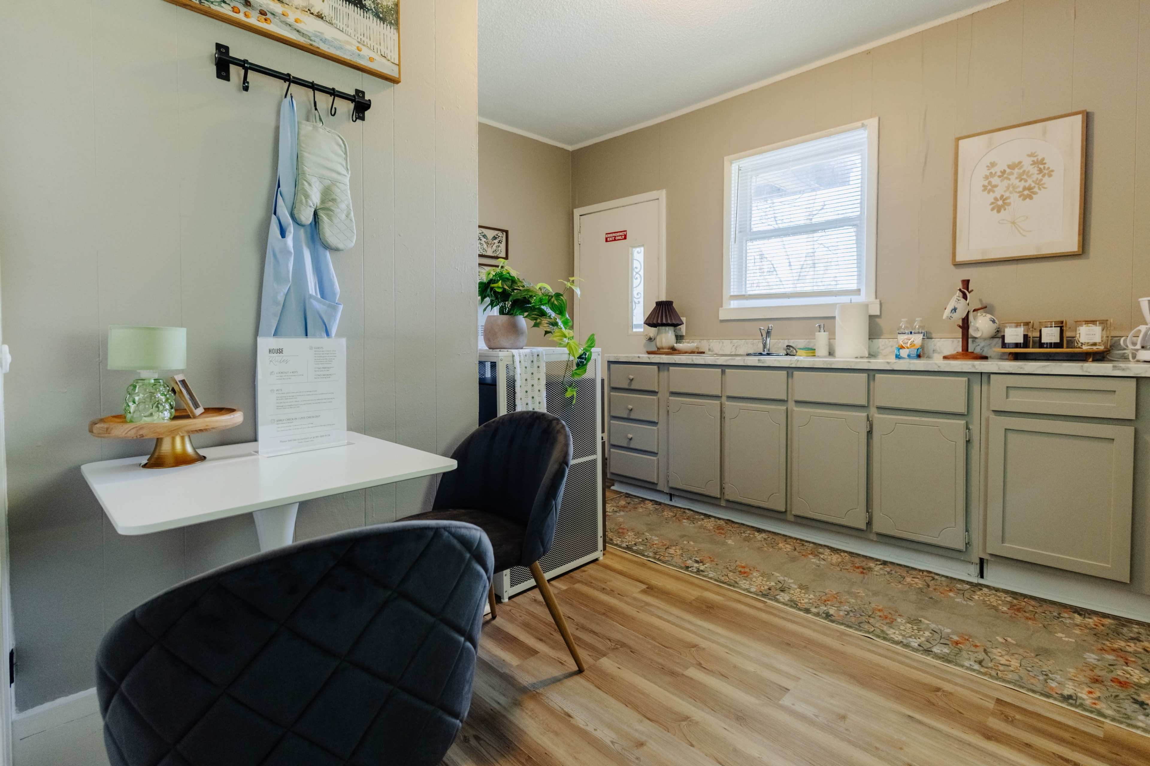 The image shows a cozy kitchen space featuring a small table with two chairs, a counter with cabinets, and a window letting in natural light.
