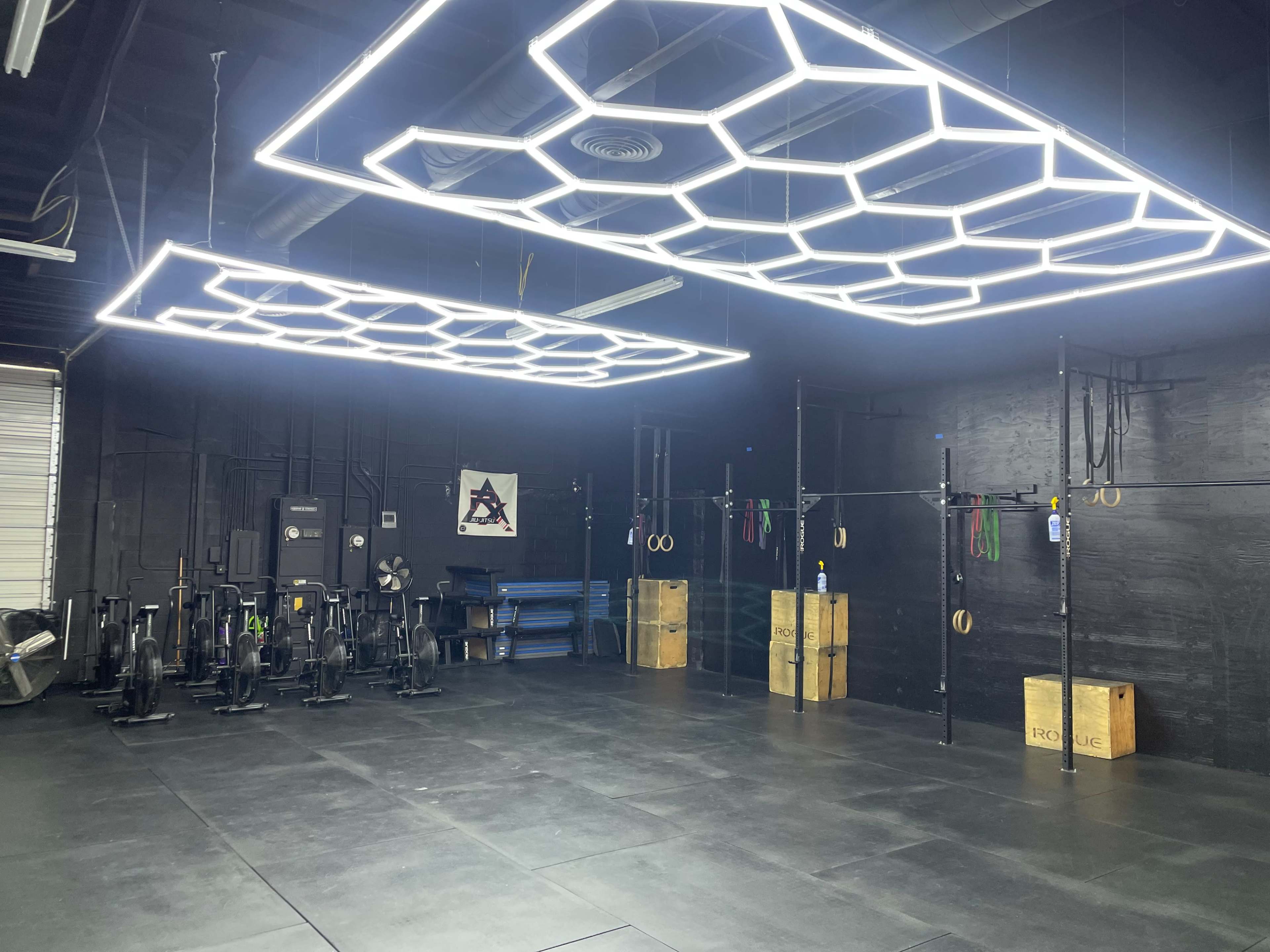A well-lit gym featuring honeycomb-patterned fluorescent lights, exercise equipment, and a large open workout area with wooden boxes.