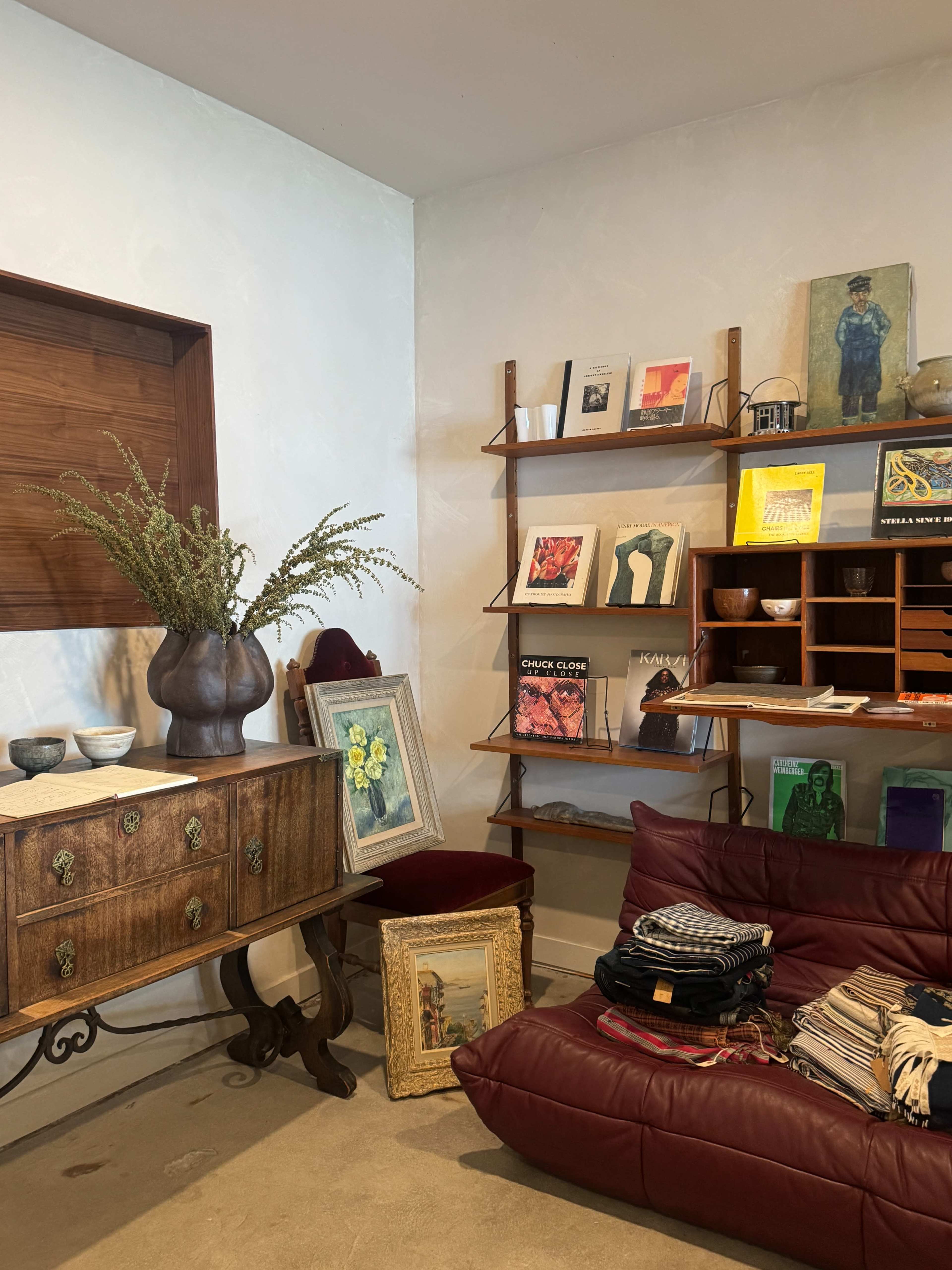 The image shows a cozy interior featuring a wooden cabinet, a red leather couch, a bookshelf with art pieces, and decorative items arranged around the space.
