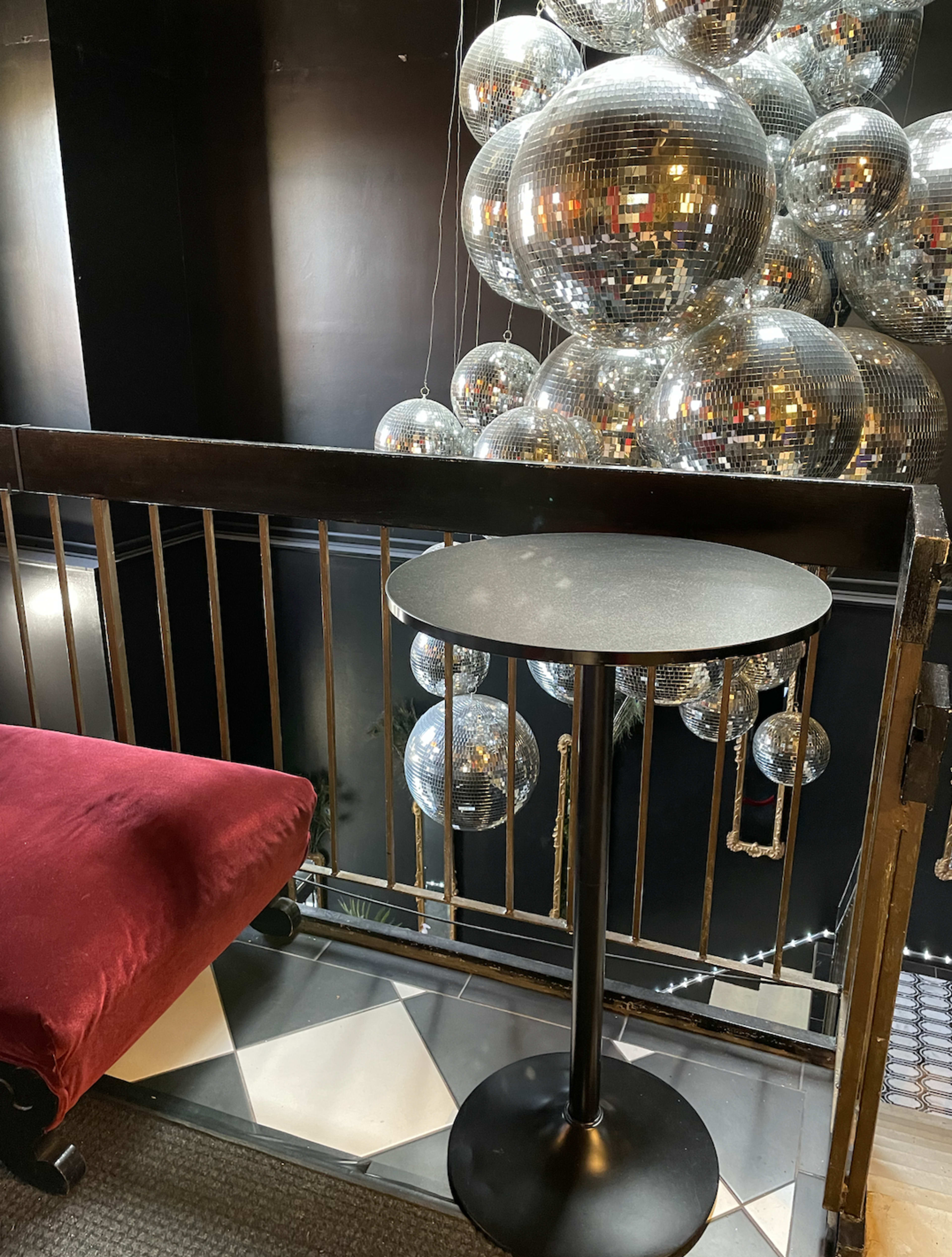 A small table stands next to a red upholstered seat, overlooking a collection of large reflective disco balls hung above.
