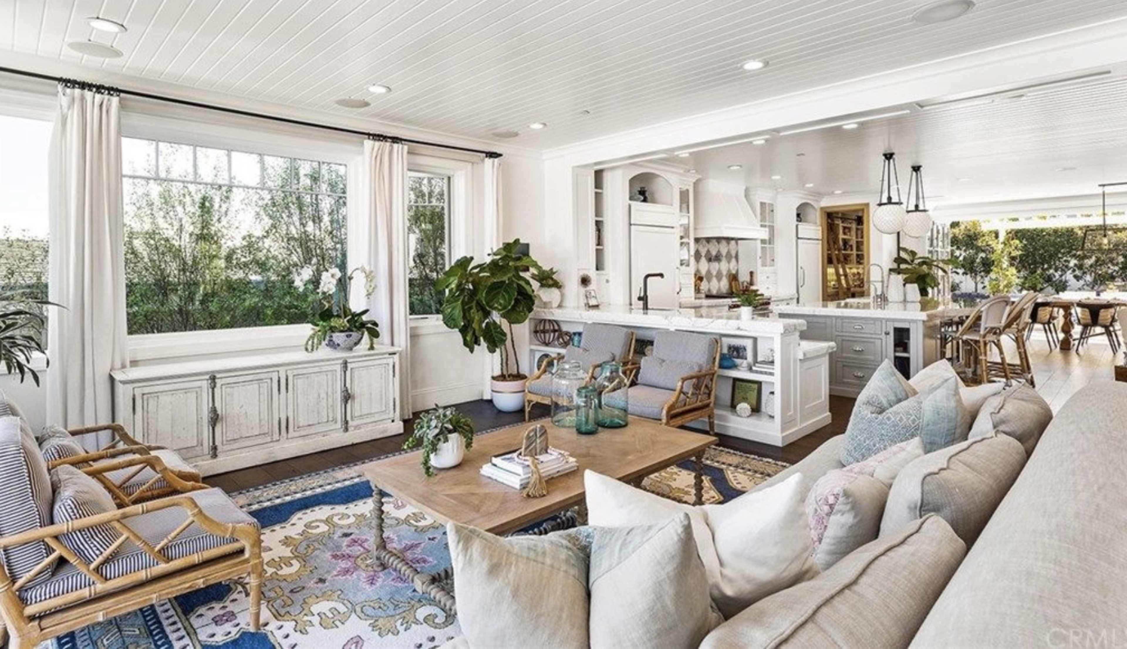 A bright, open living room with a mix of comfortable seating, a wooden coffee table, and large windows overlooking greenery.