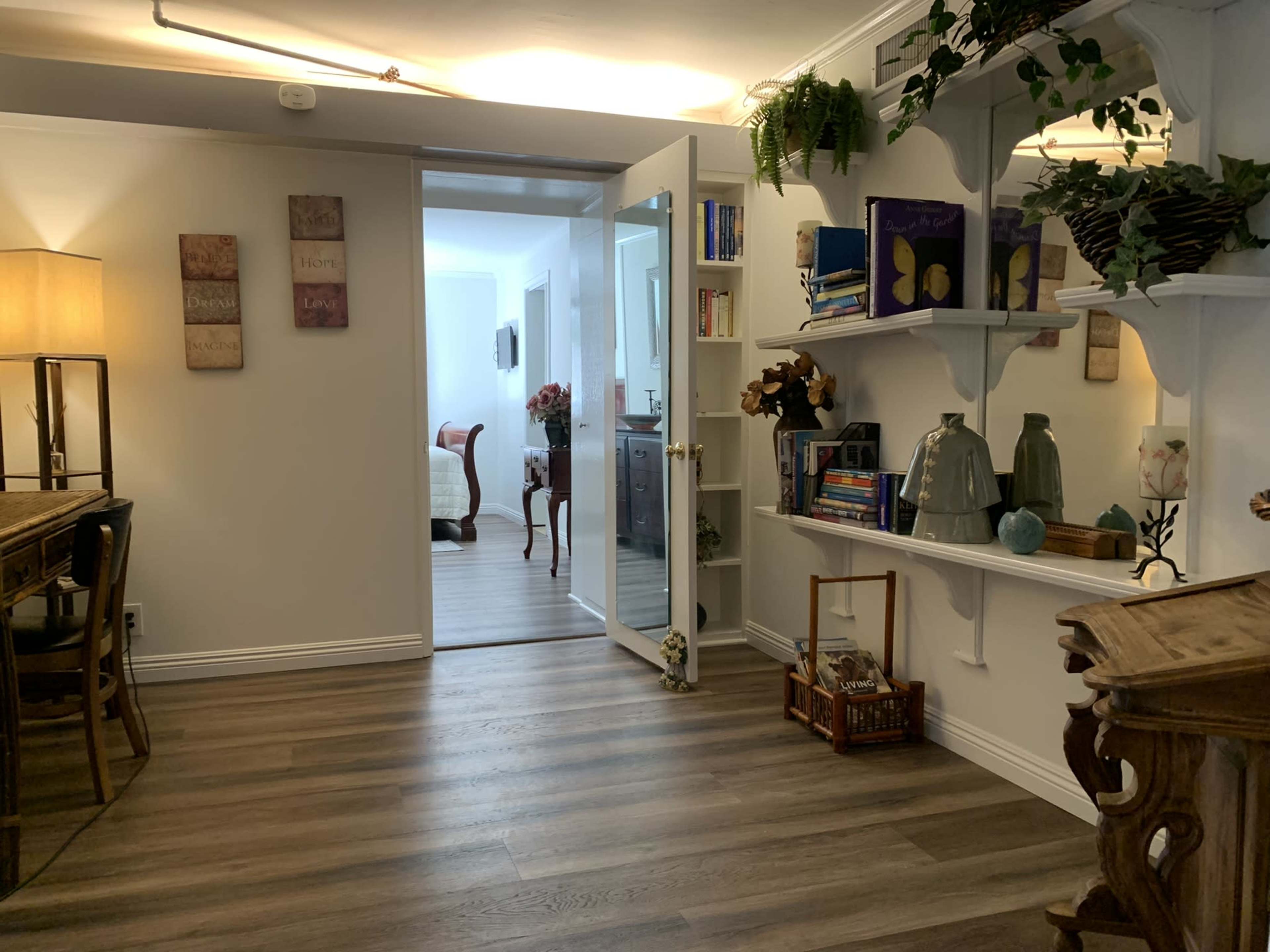 A well-lit interior space with a wooden dining table, bookshelves lined with decorative items, and a doorway leading to another room.