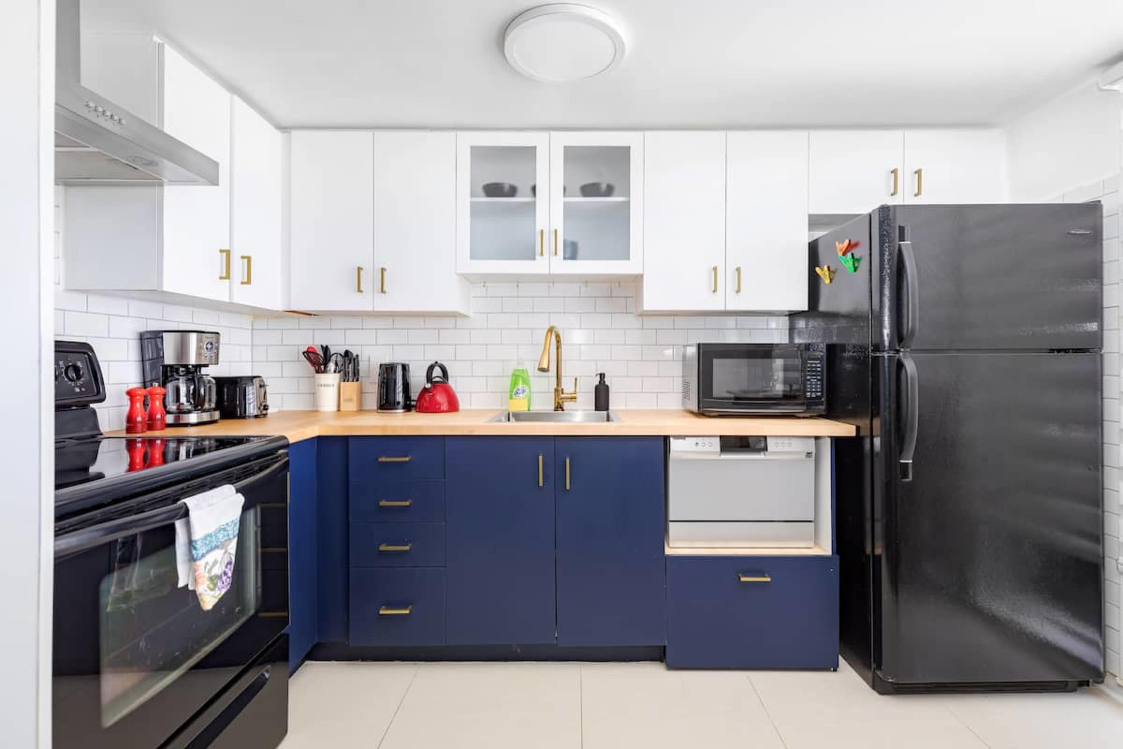 A modern kitchen features white cabinets with gold handles, a blue base cabinet, stainless steel appliances, and a countertop with various kitchen items.