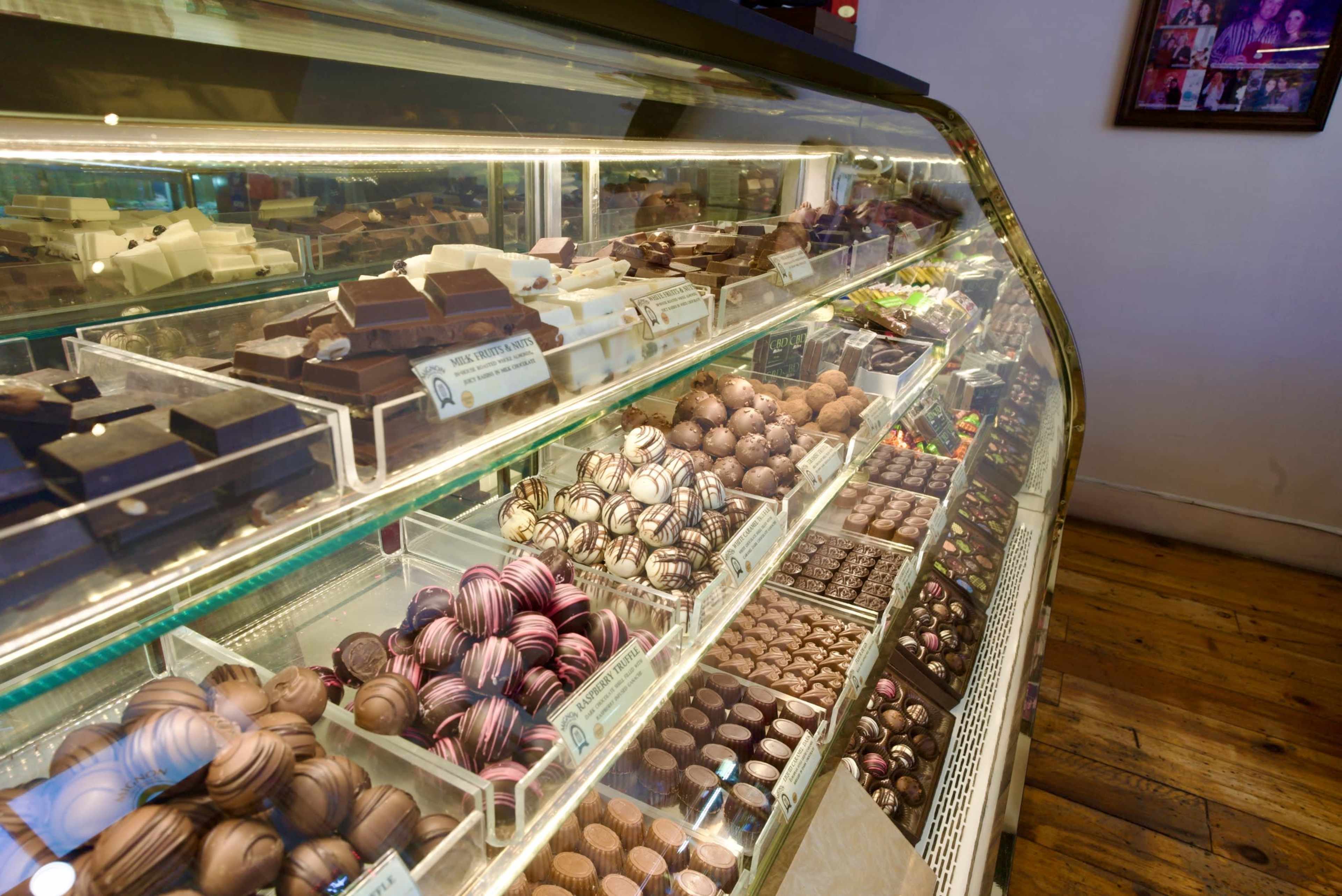 The image shows a display case filled with an assortment of chocolates, including dark chocolate bars, chocolate-covered sweets, and various pralines.