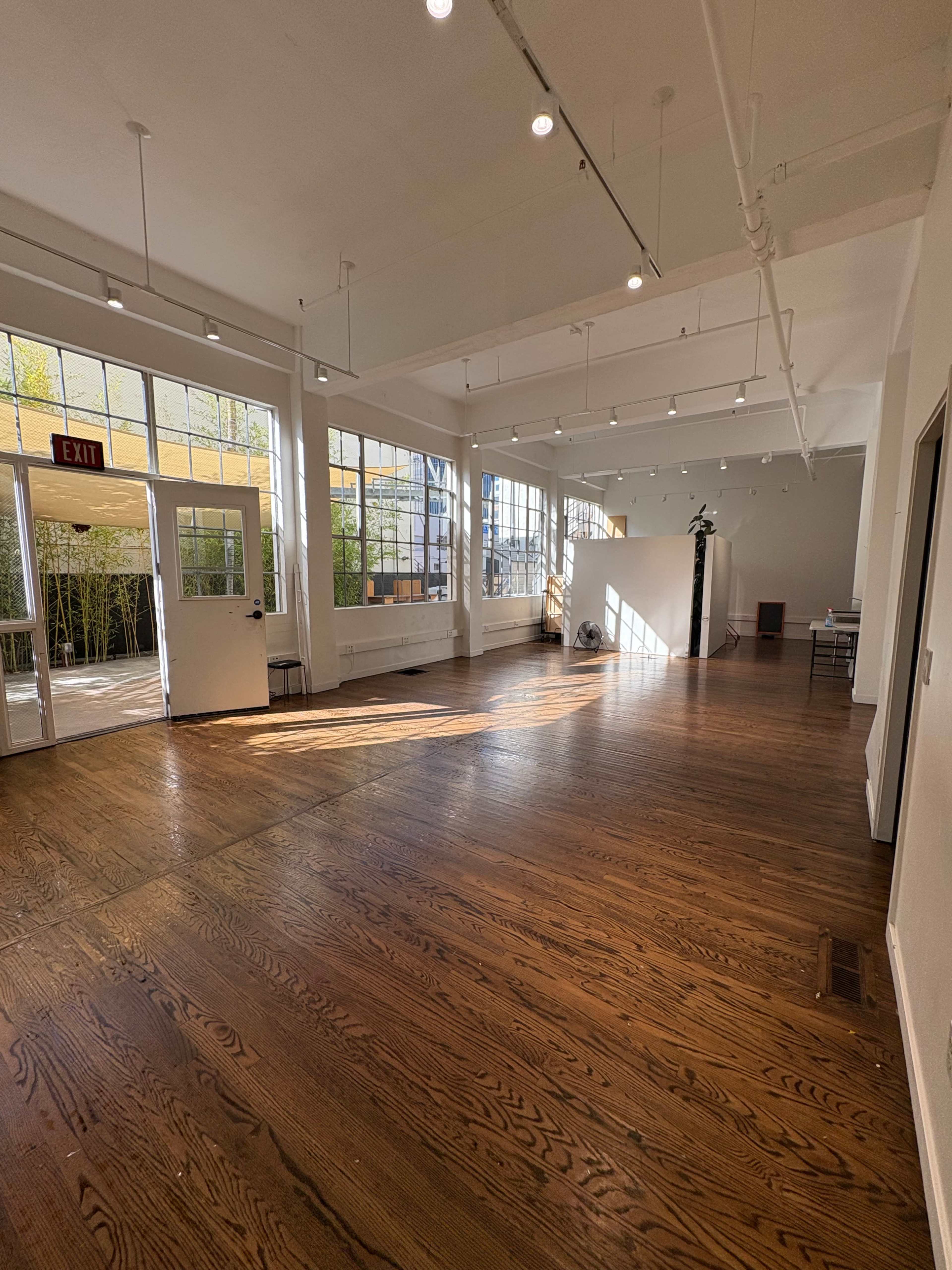 The image depicts a spacious, well-lit interior of an empty room with large windows and wooden flooring.