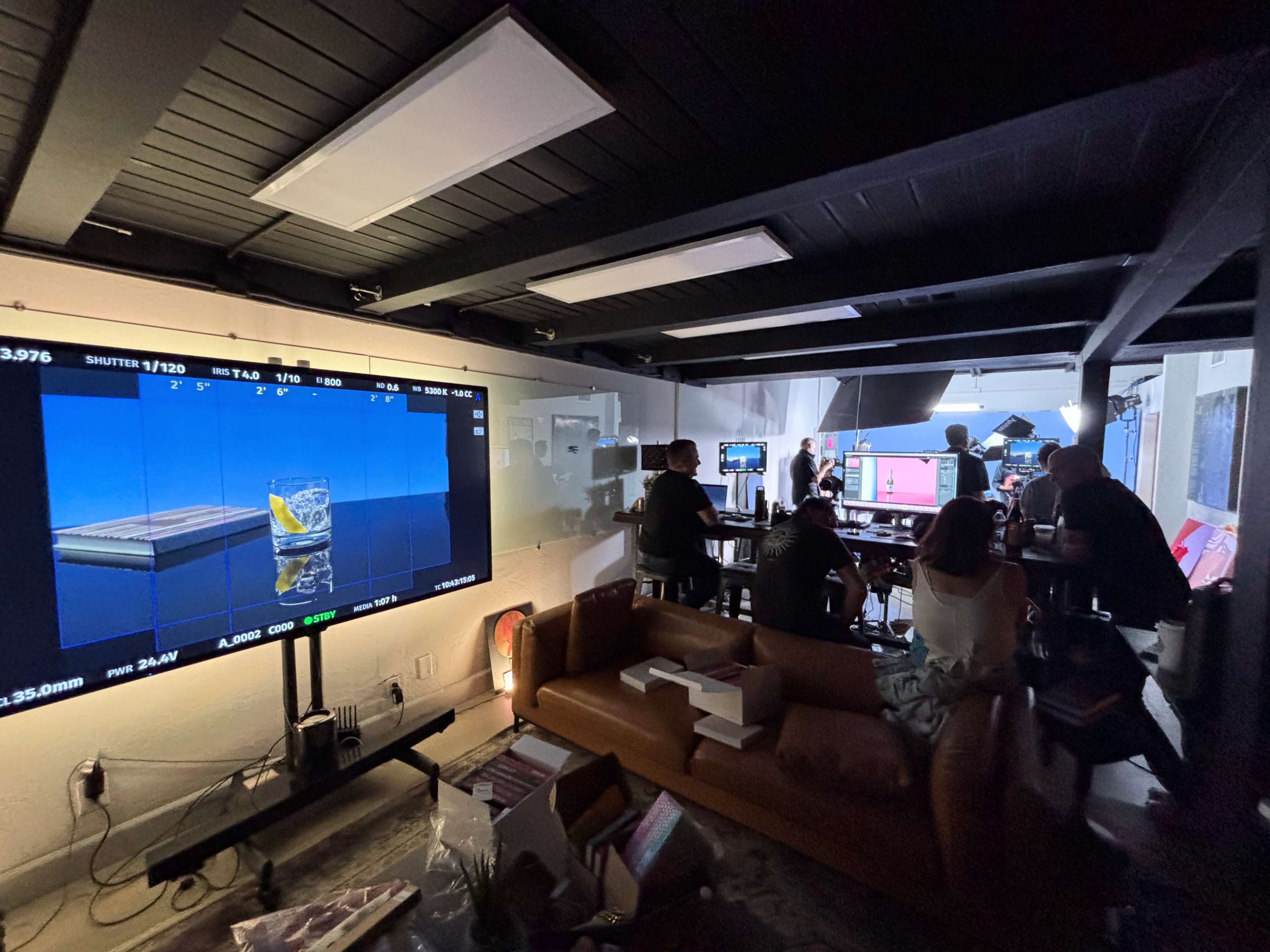 A group of people is gathered in a studio, working on a video production, with equipment and a large screen displaying camera settings.