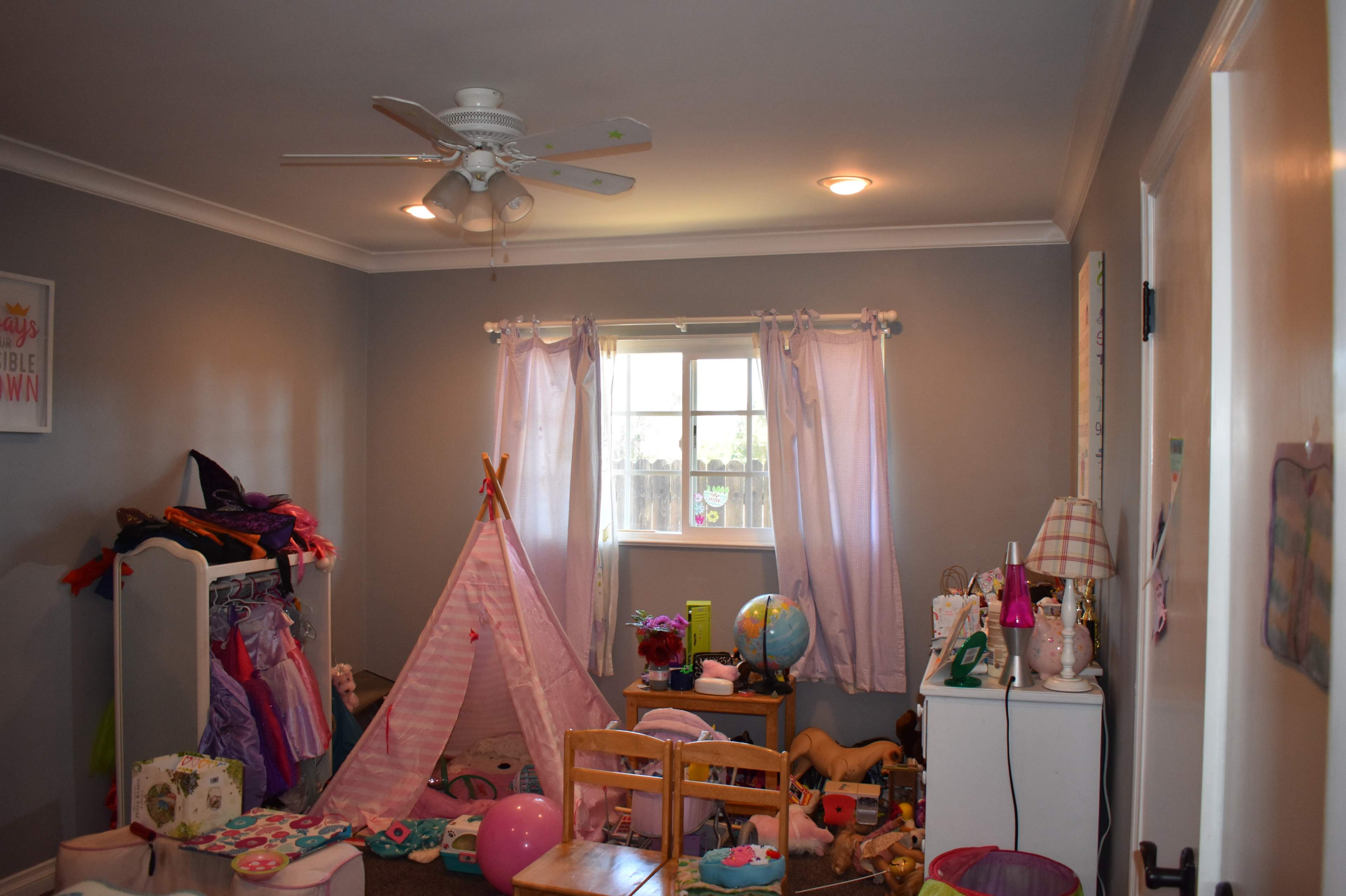 A children's bedroom features a play tent, a variety of toys scattered throughout, and a window with sheer curtains.