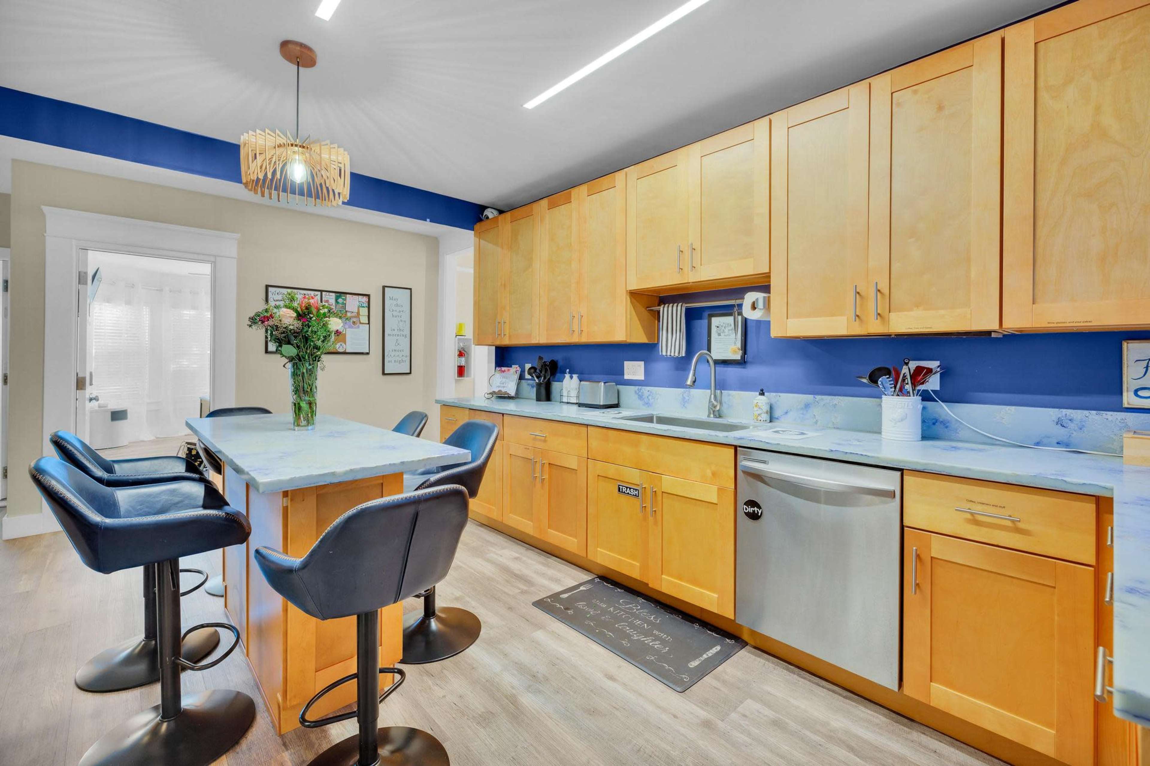 A modern kitchen with wooden cabinets, a blue accent wall, a countertop with seating, and stainless steel appliances.