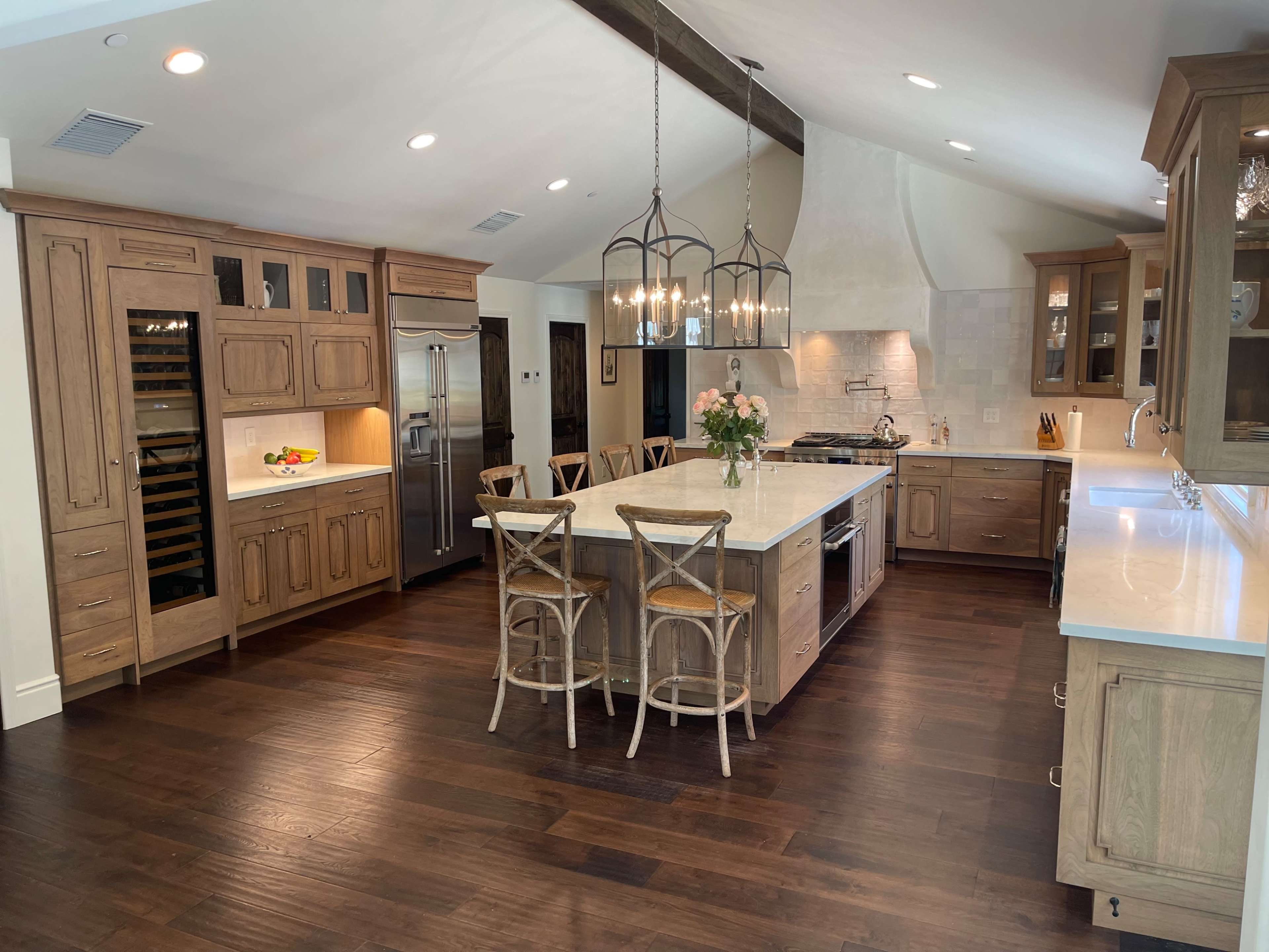 The kitchen features wooden cabinetry, an island with seating, a stainless steel refrigerator, and pendant lighting.
