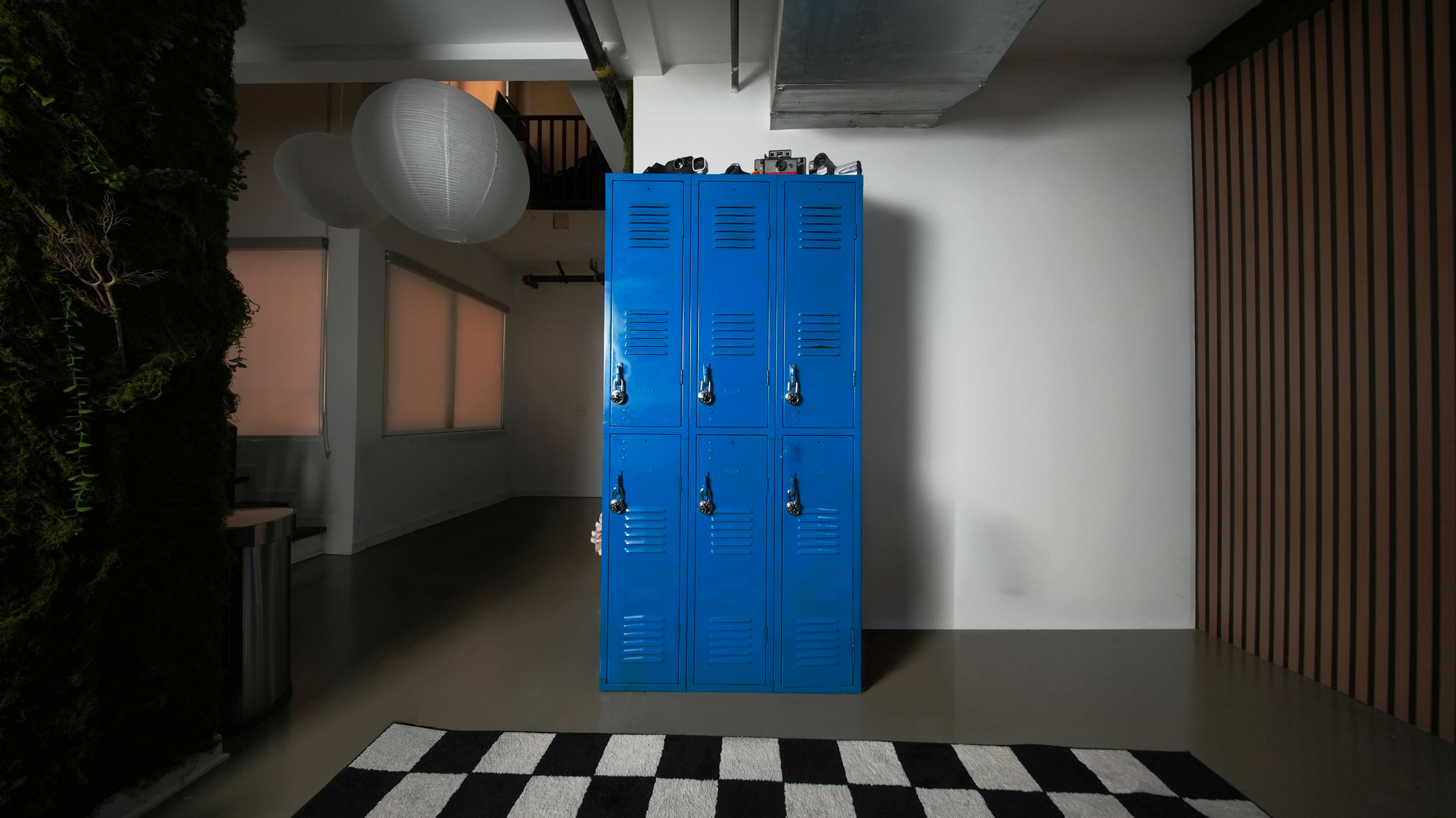 The image shows a blue metal locker cabinet against a white wall, with a striped black and white rug on the floor in front of it.