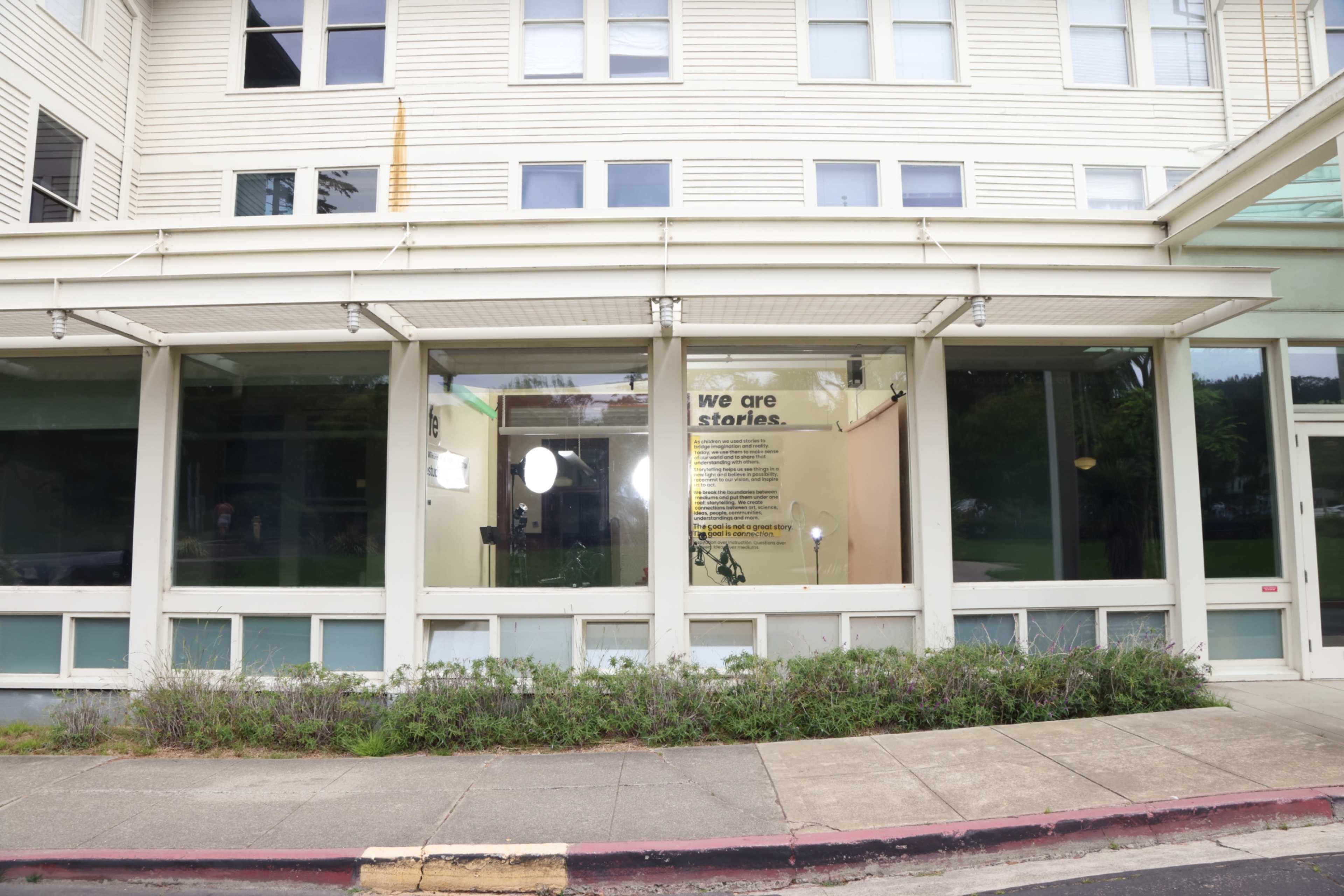 The image shows a storefront with large windows and a wall displaying text that reads "we are stories."