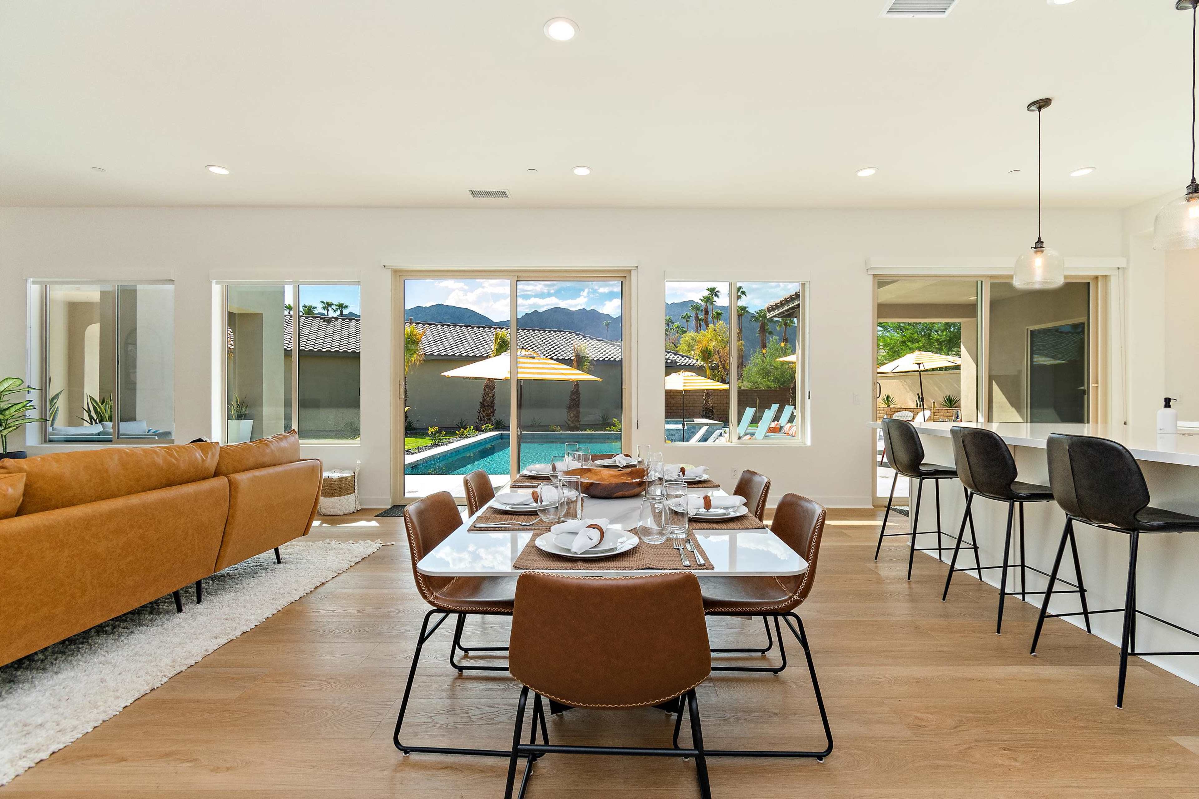 A modern dining area with a large table set for a meal, overlooking a pool and outdoor space through large windows.