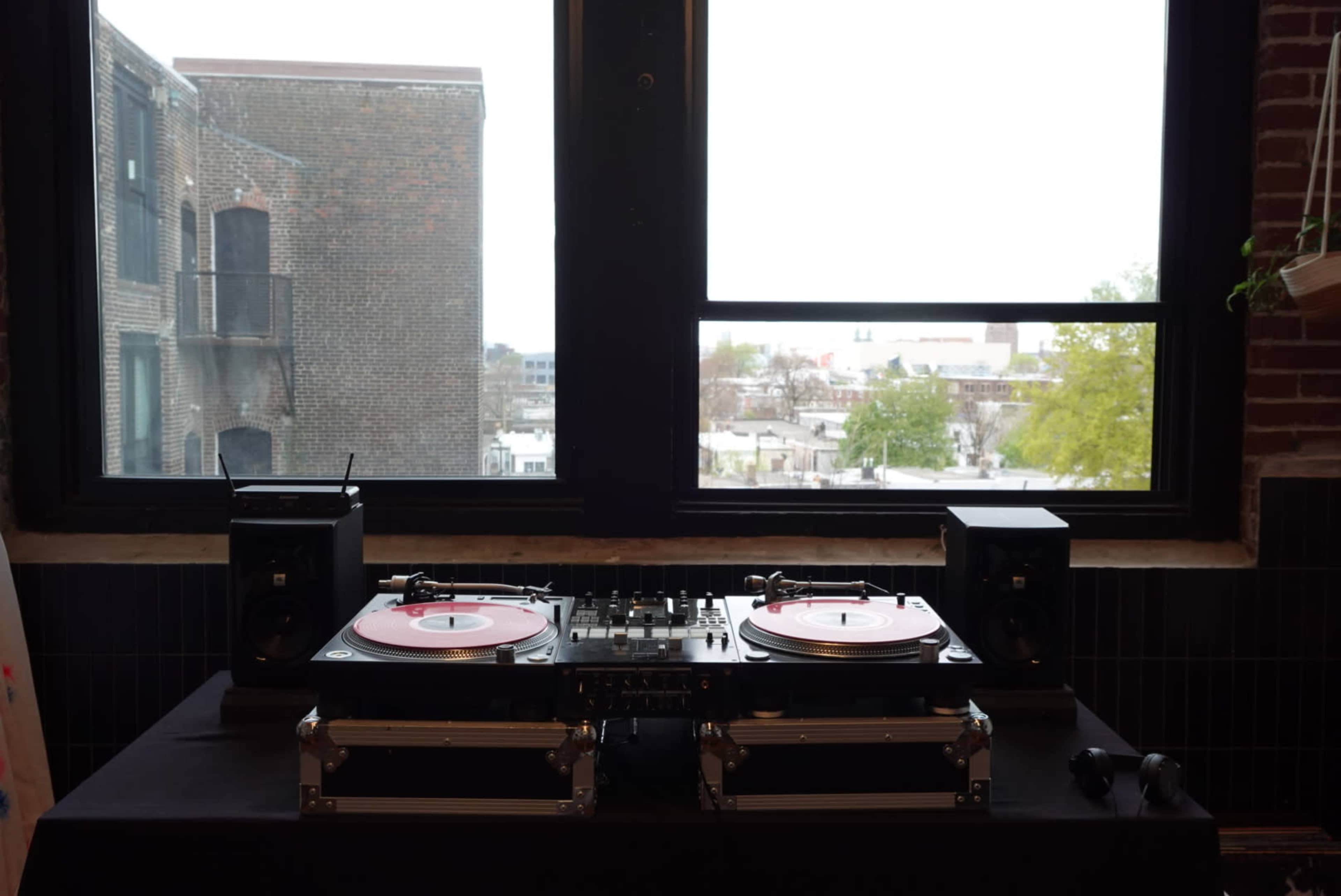 A pair of turntables and speakers are set up on a table near a large window overlooking a cityscape.