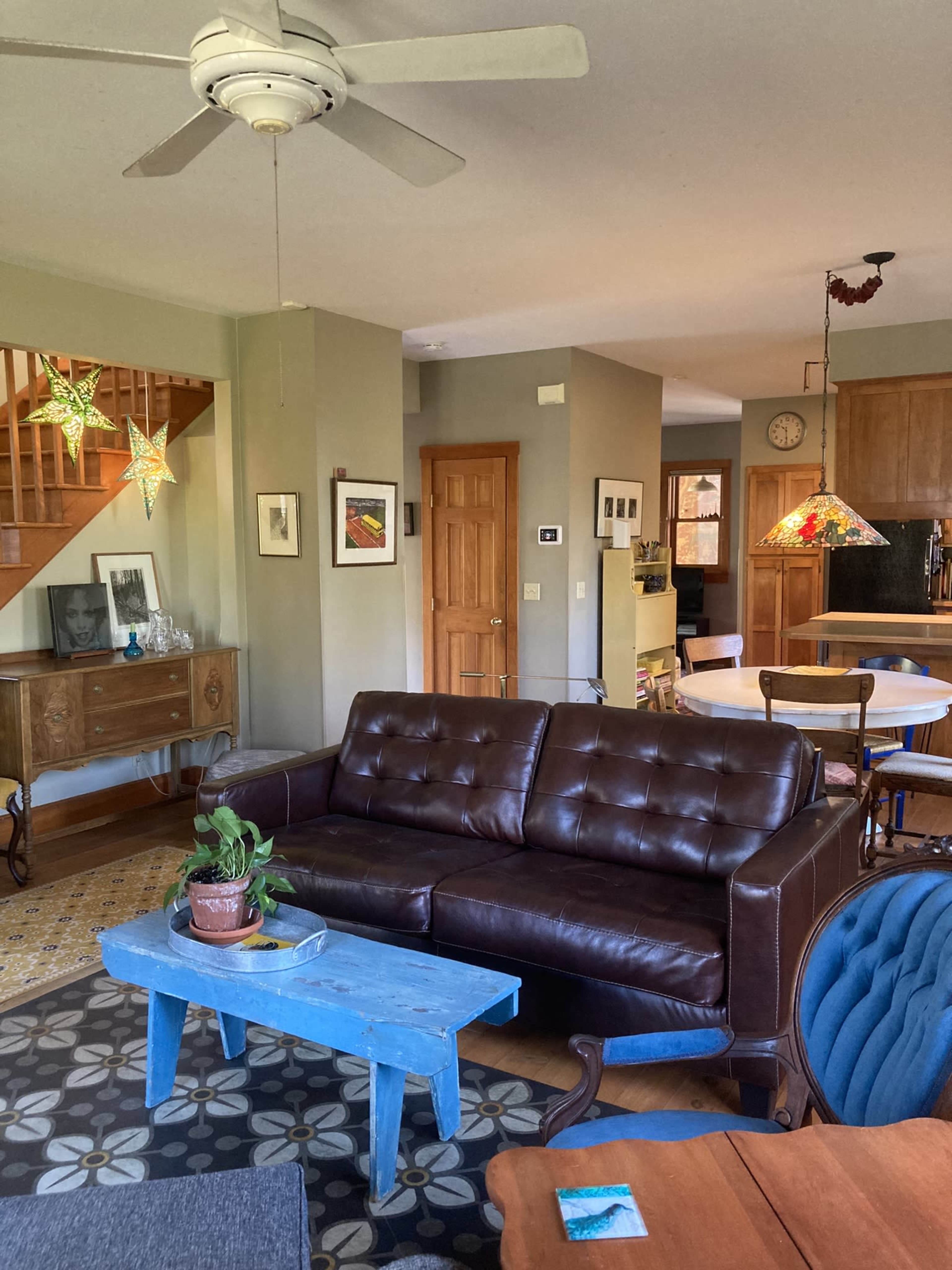 The image shows a living room with a brown leather sofa, a blue coffee table, and various light fixtures hanging from the ceiling, including star-shaped designs.