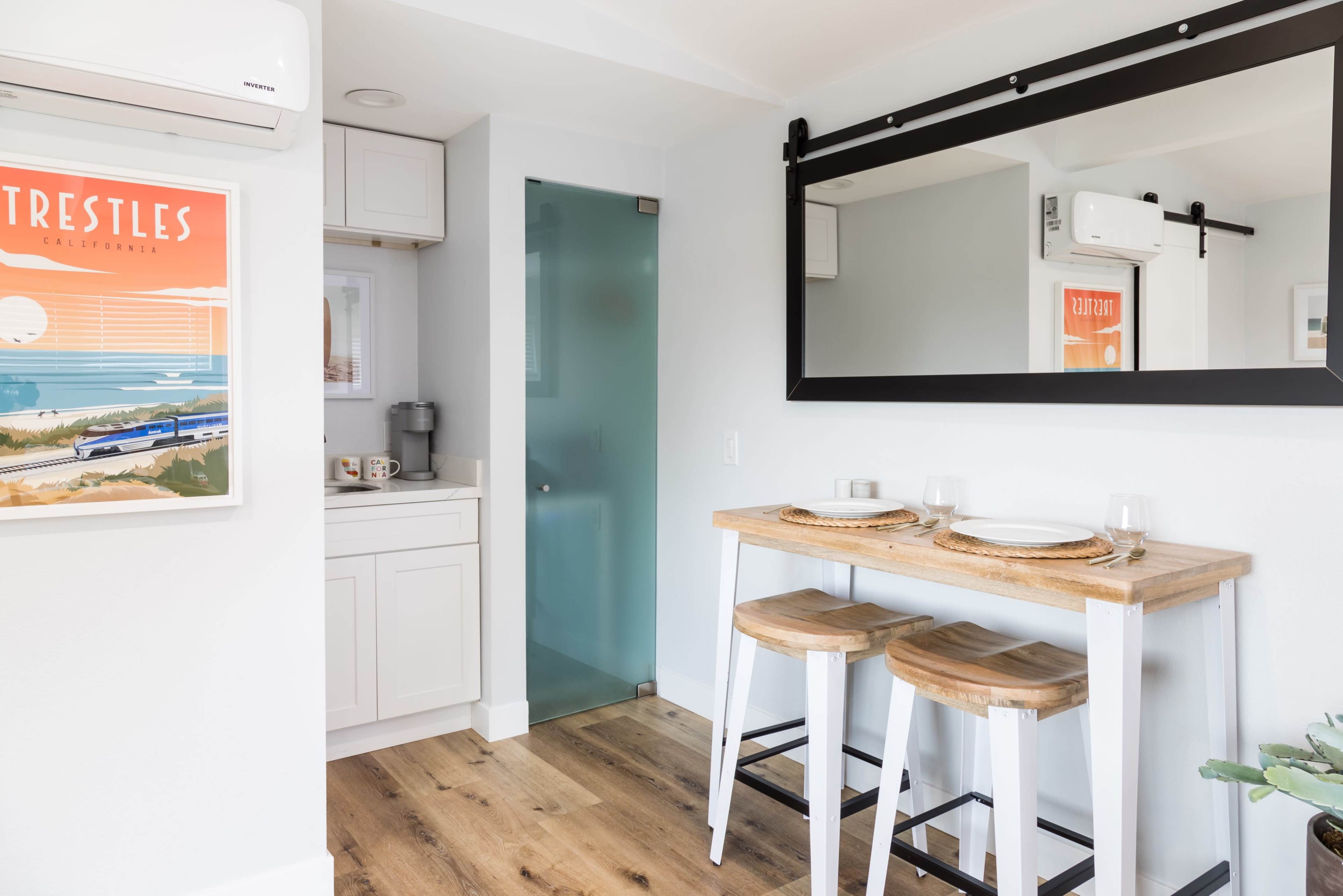 A small kitchen area features a bar table with two stools, a kitchenette, and a mirror above the table.