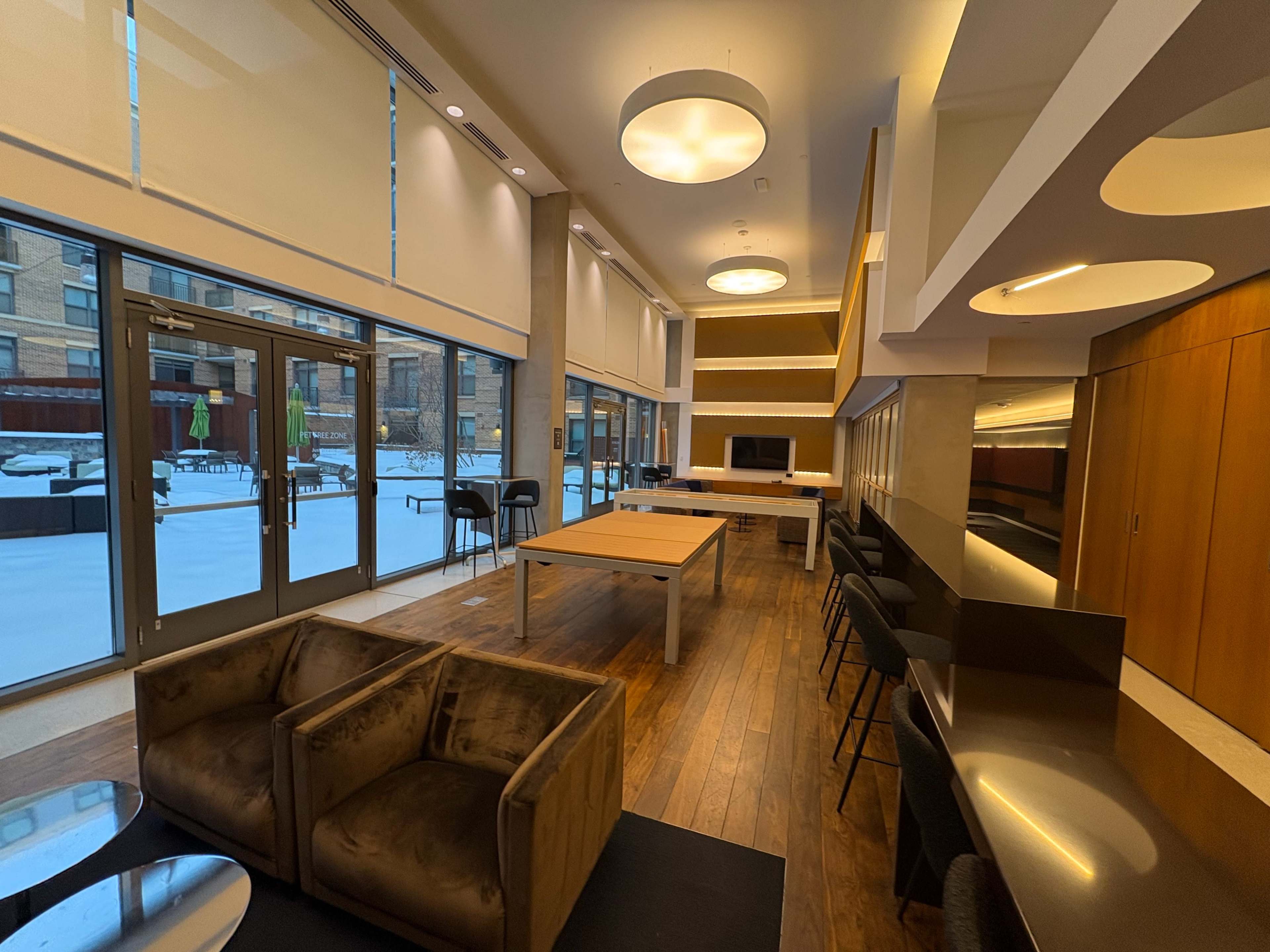 The image shows a modern indoor lounge area with seating, tables, and large windows showcasing a snowy outdoor view.