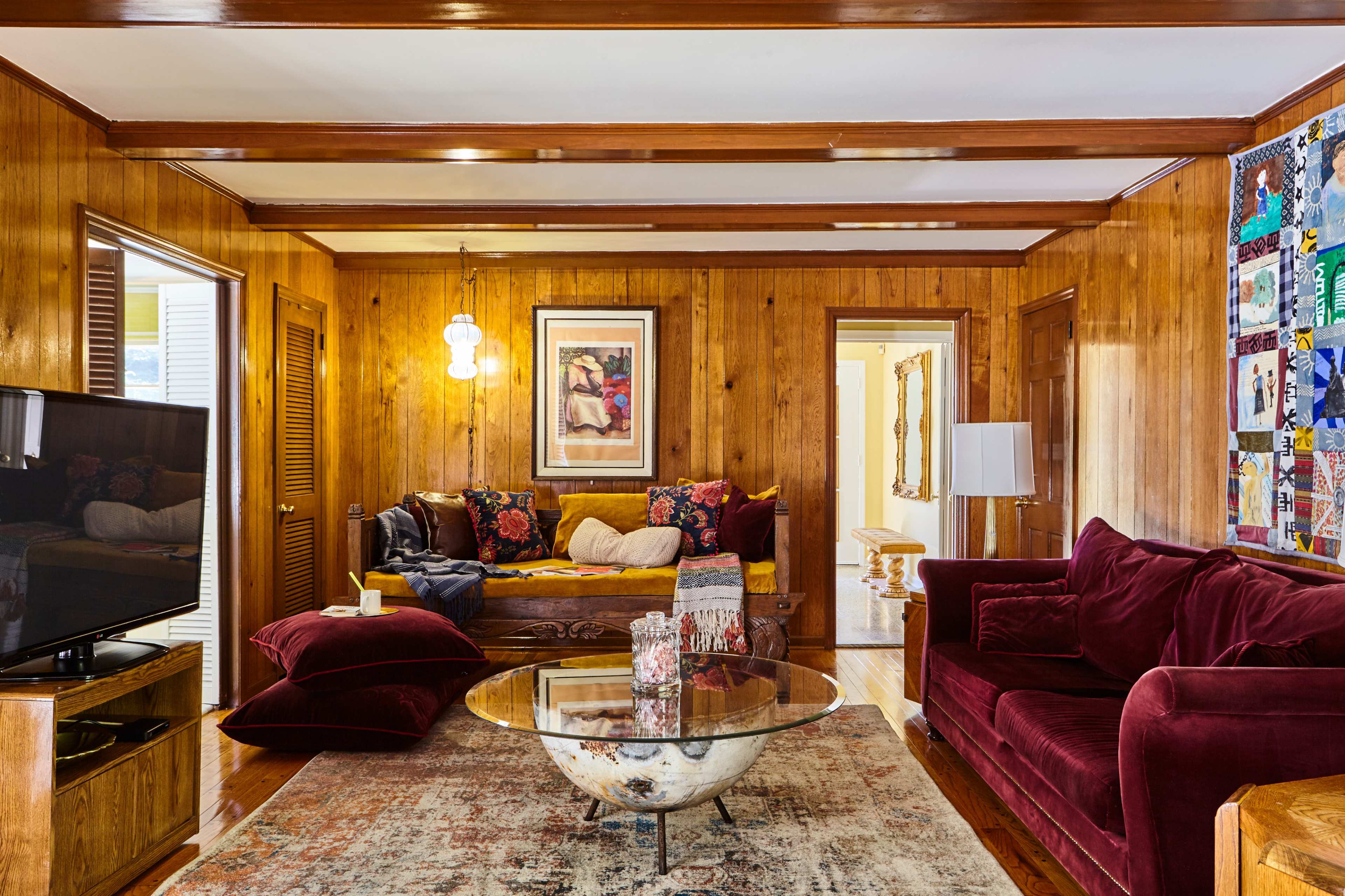 The living room features wooden wall paneling, a glass coffee table, a plush red couch, and a television.