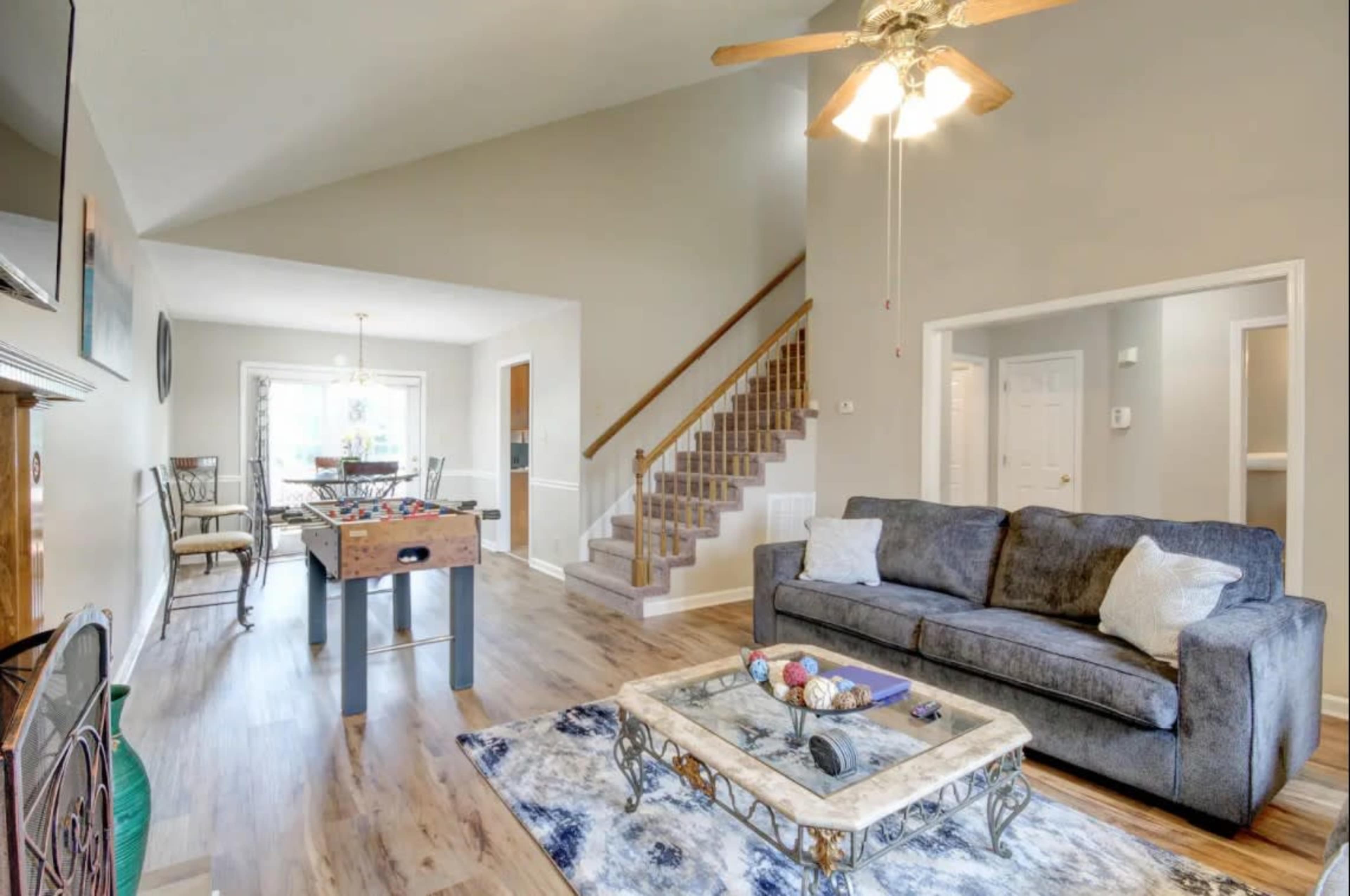 A living room with a gray sofa, a coffee table with decorative items, and a staircase leading to another level, adjacent to a dining area.