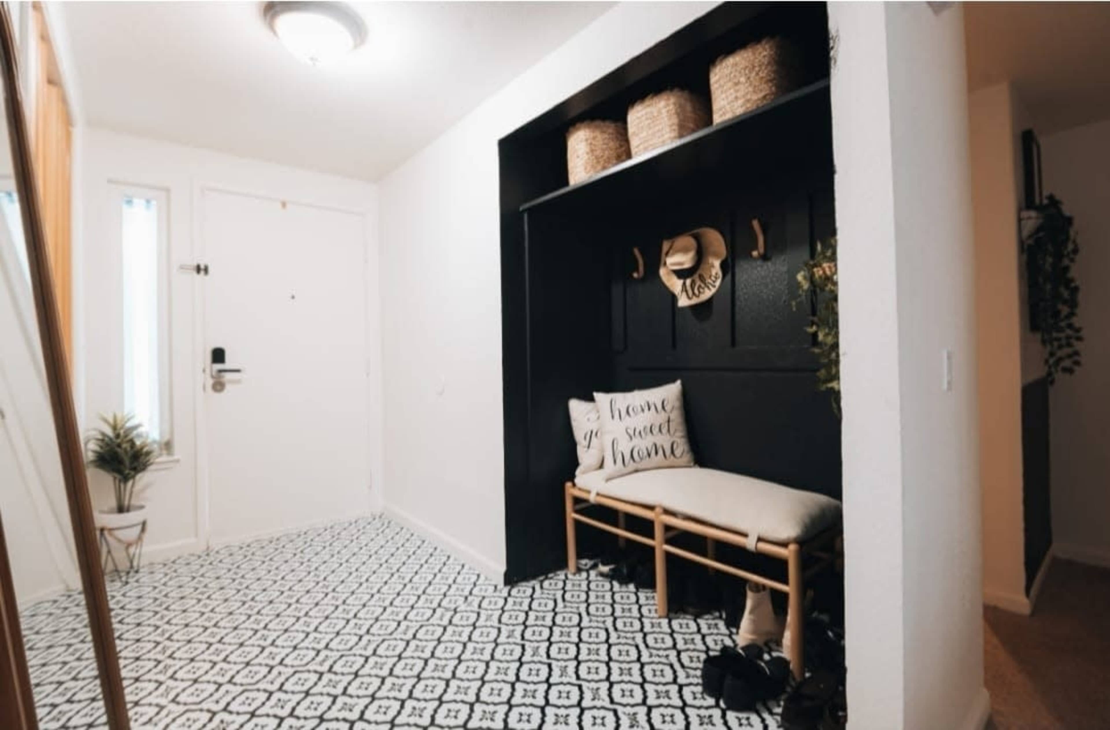 The image shows a modern entryway featuring a bench with a decorative pillow, storage baskets on a shelf, and a patterned tile floor.