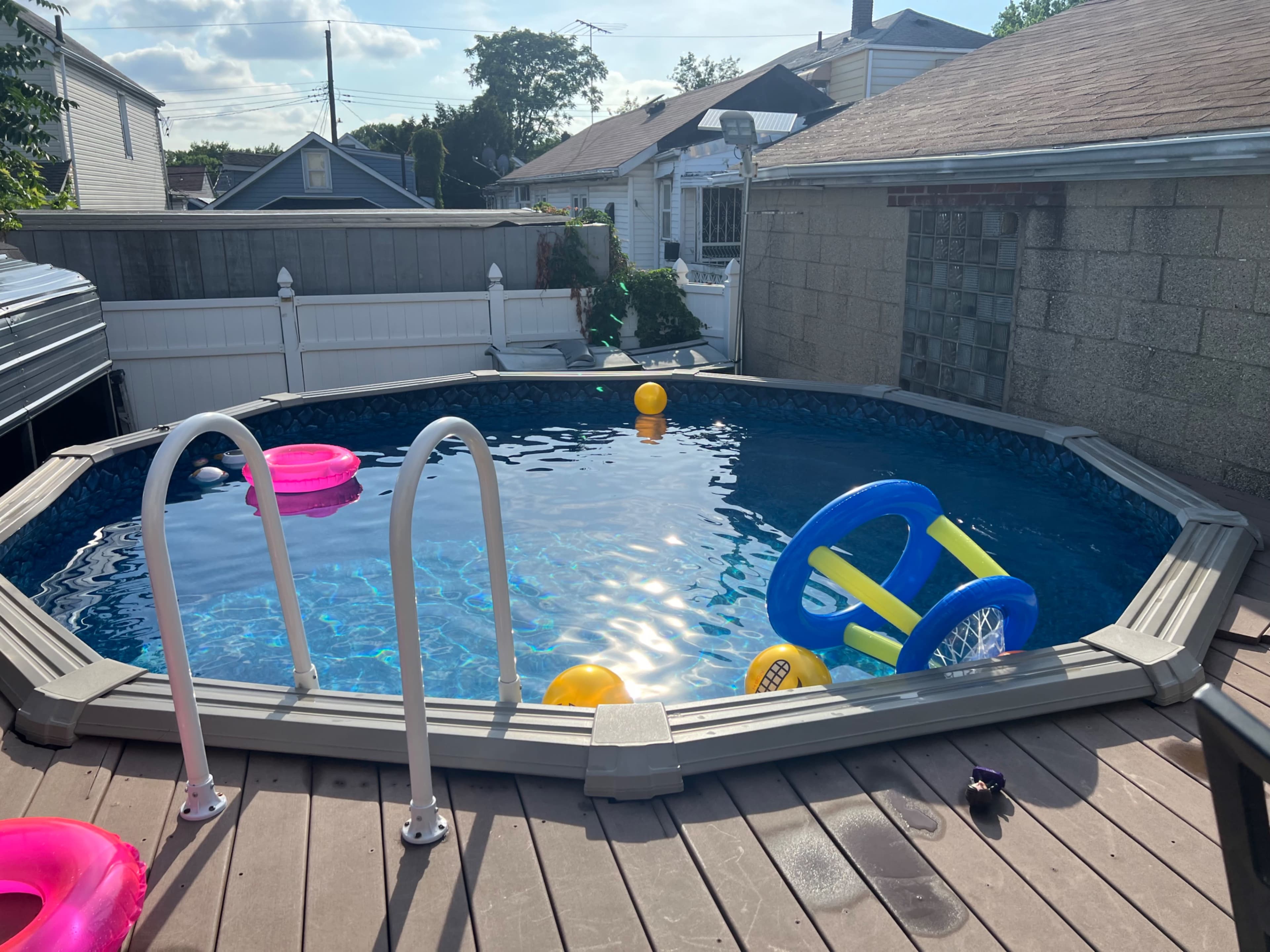 A circular above-ground pool filled with water and colorful inflatable floaties is surrounded by a wooden deck.